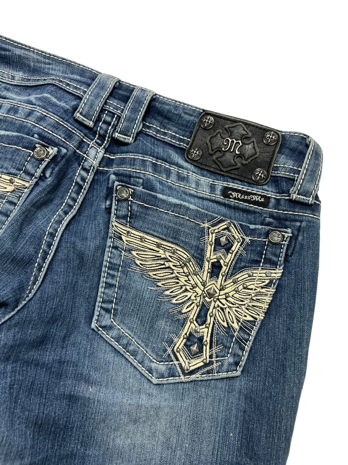 Die Miss Me Low Rise Boot Jeans von ZAZA resell hat blauen Denim, dekorative Nähte auf der Gesäßtasche mit einem gestickten Kreuz und Flügeln sowie einen schwarzen Lederaufnäher mit einem stilisierten "M". Siehe Labelgröße und Bundweite für die Größenbestimmung.