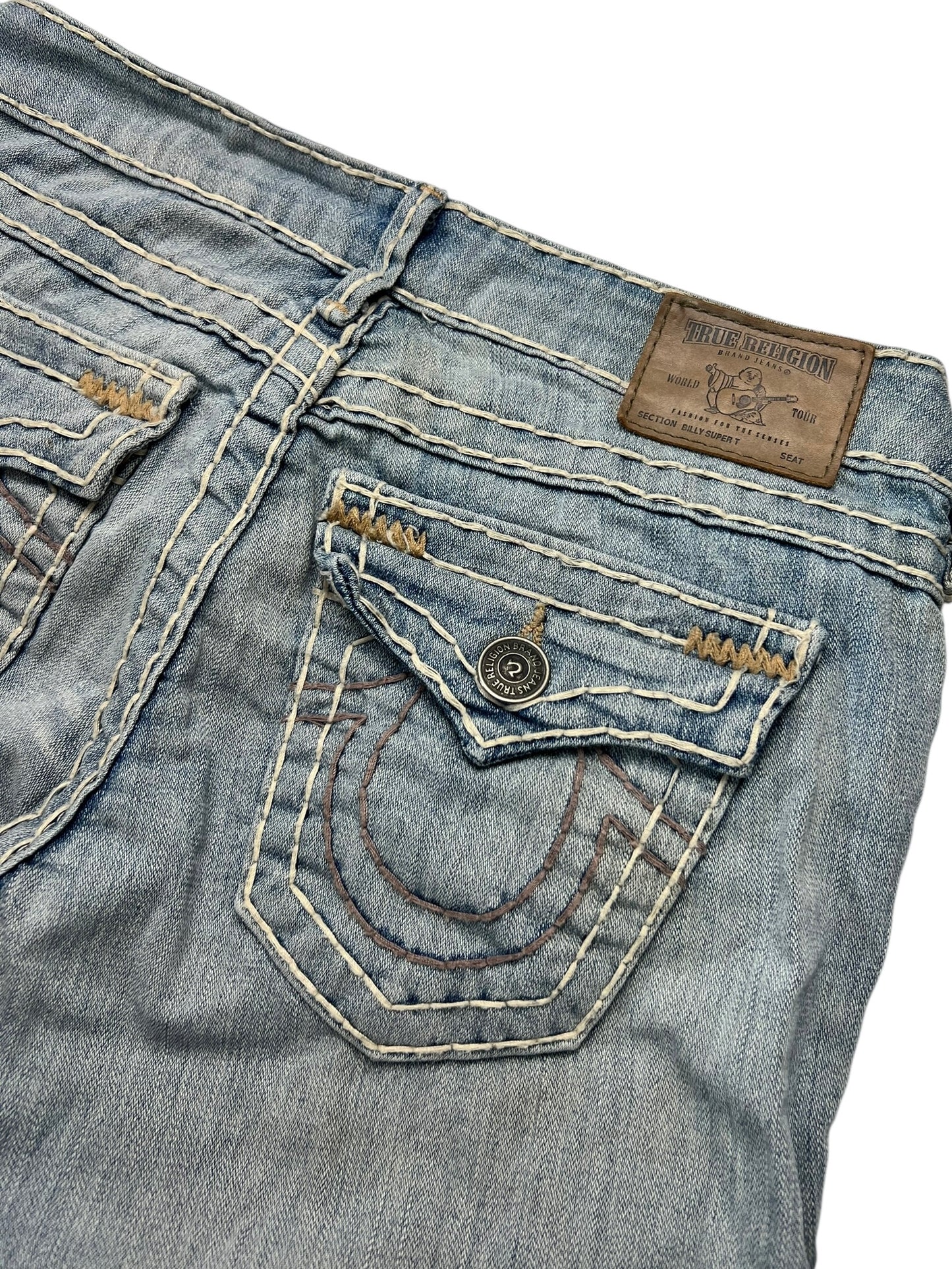 Nahaufnahme der Gesäßtasche der hellblauen True Religion Billy Super T – Low Rise Straight Jeans (W26 x L28) von ZAZA Resell, mit weißen Nähten, einer geknöpften Klappe, sichtbarem braunen Markenaufnäher aus Leder und Größenetikett über der Tasche.