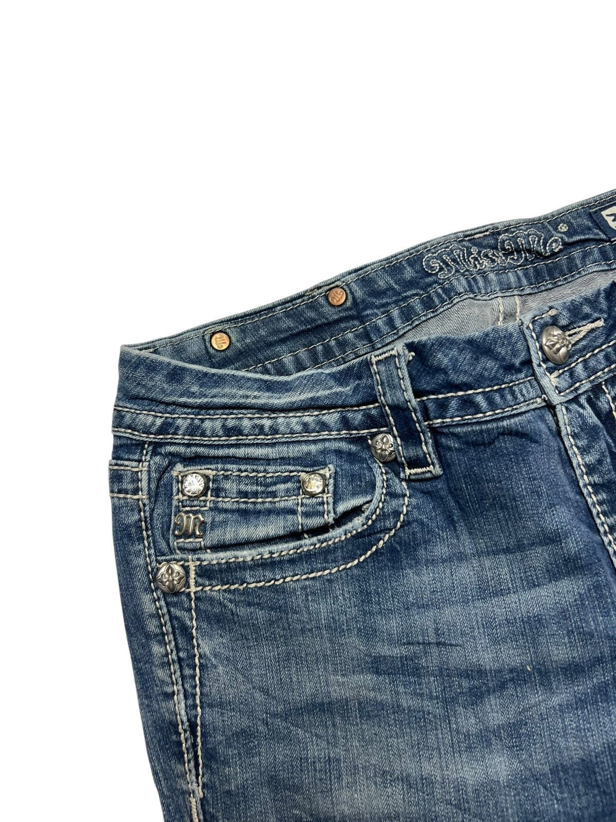 Nahaufnahme der Miss Me Mid Rise Boot Jeans von ZAZA resell in Größe 30 (M) aus blauem Denim mit weißen Nähten, Metallnieten, bestickten Taschen, einer kleinen Vordertasche, Gürtelschlaufen und einem gut lesbaren Größenetikett.