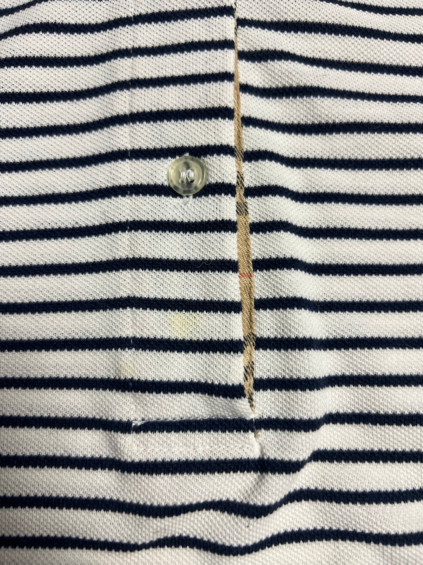 Nahaufnahme eines Burberry Polo Shirts | S von ZAZA resell, weiß mit schwarzen Querstreifen. Mit durchsichtigem Plastikknopf, aufgeknöpfter Knopfleiste, sichtbaren Nähten und beigem Innenfutter. Zustand 8/10. Maße in Zentimetern auf Anfrage.