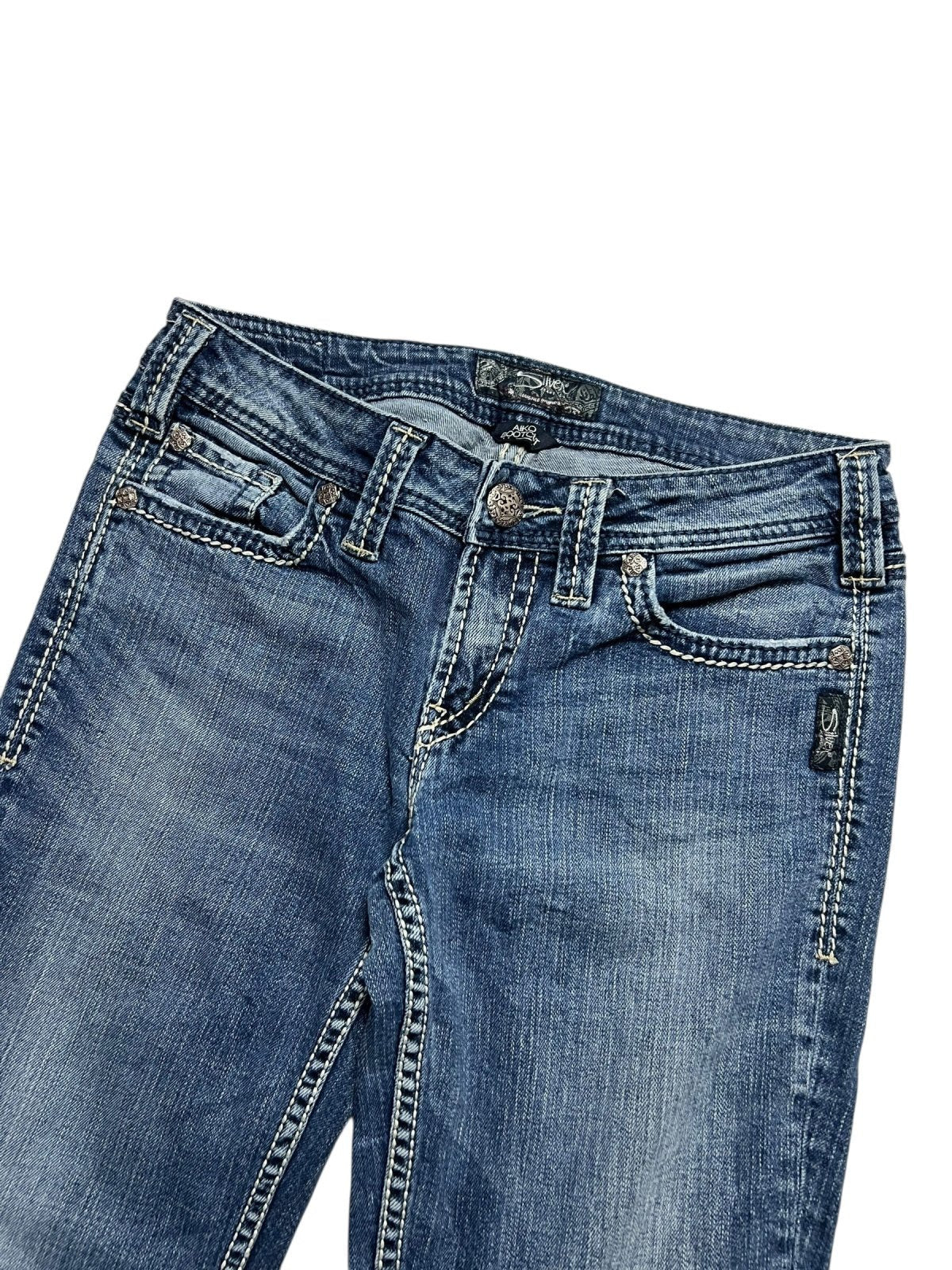 Die Silver Jeans Low Rise Boot in Größe 29 (M) von ZAZA resell hat blauen Denim, weiße Kontrastnähte, Taschen vorne, Gürtelschlaufen und einen Metallknopfverschluss. Bundweite und Labelgröße sorgen für die perfekte Passform. Abgebildet auf weißem Hintergrund.