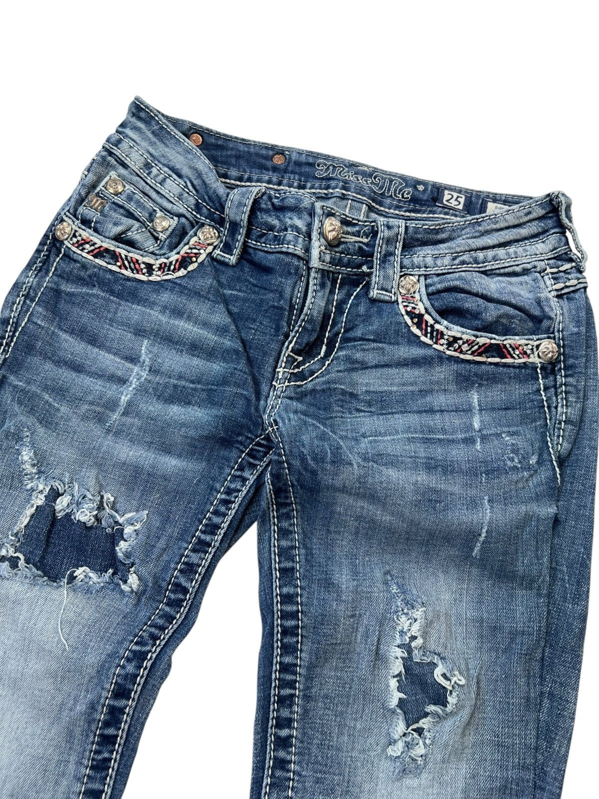 Die Miss Me Low Rise Straight Jeans von ZAZA resell in Größe 25 (XS/S) hat einen Used-Look mit blauem Distressed-Denim, ausgefransten Löchern an beiden Beinen, Nähten an den Vordertaschen und einer detaillierten Bundweite. Ausgestellt vor einem weißen Hintergrund.