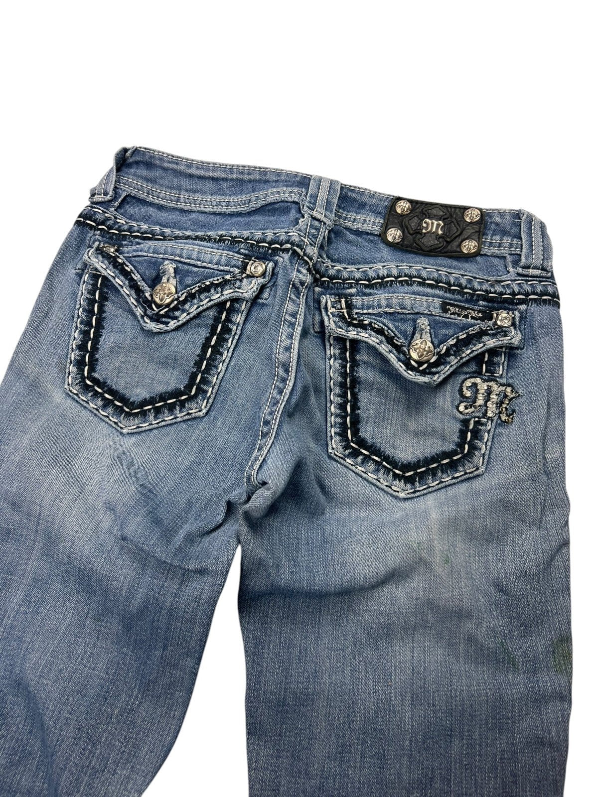 Die Miss Me Mid Rise Boot Jeans von ZAZA Resell in W26 x L29 besteht aus blauem Denim, hat dekorative Nähte, verzierte Klappen an den Gesäßtaschen, metallische Knöpfe, einen M-Logo-Patch über der rechten Tasche und eine stylische Beinöffnung für einen modernen Touch.