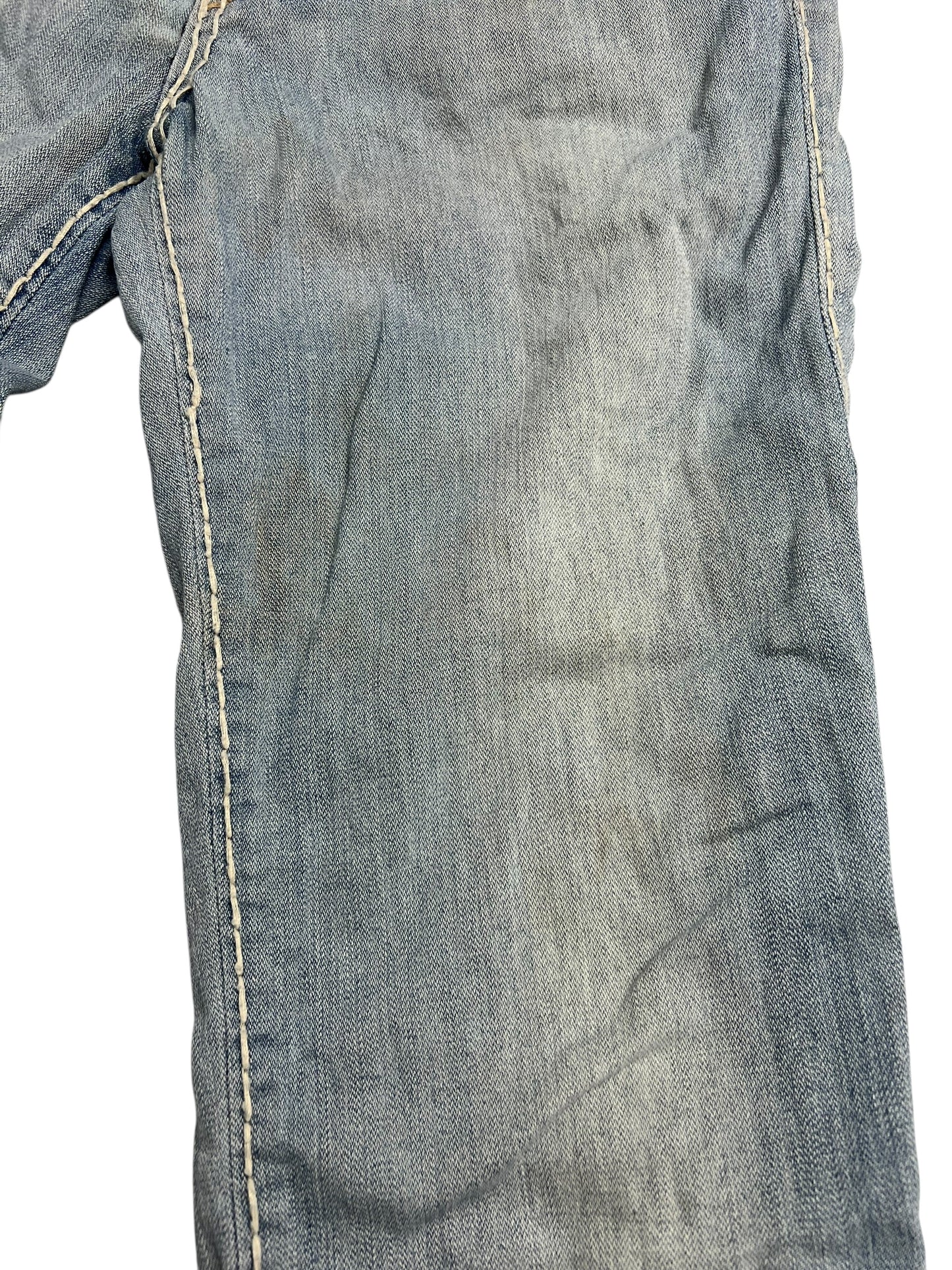 Nahaufnahme eines verblichenen blauen Hosenbeins der Marke True Religion Billy Super T (B26 x L28) von ZAZA Resell mit abgenutztem Stoff, weißen Nähten, Flecken und leichter Verfärbung.