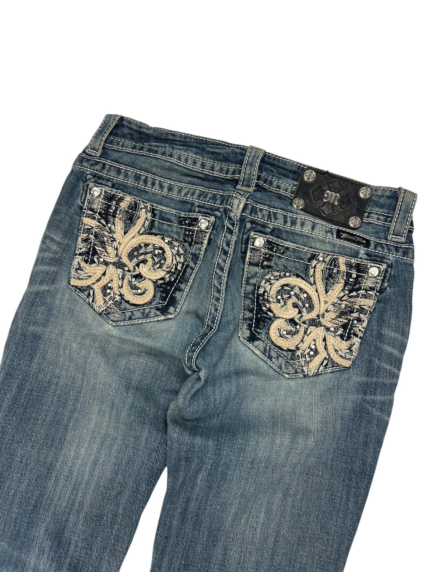 Die Miss Me Low Rise Straight Jeans (Größe 27/S) von ZAZA resell ist mit dekorativen Fleur-de-Lis-Stickereien auf den Gesäßtaschen und einem schwarzen Markenpatch über der rechten Tasche versehen.
