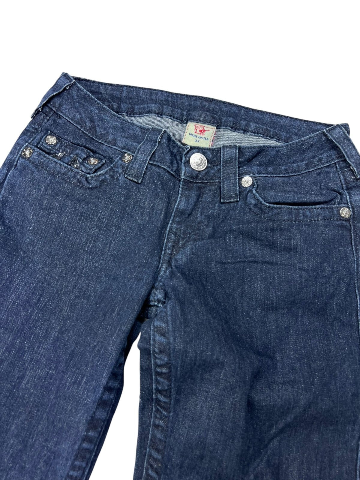 Ein Paar True Religion Low Rise Boot Jeans (W27 x L34) von ZAZA Resell, blauer Denim mit Vordertaschen, silbernen Knöpfen und einem Etikettgröße-Etikett, flach auf weißem Hintergrund liegend.