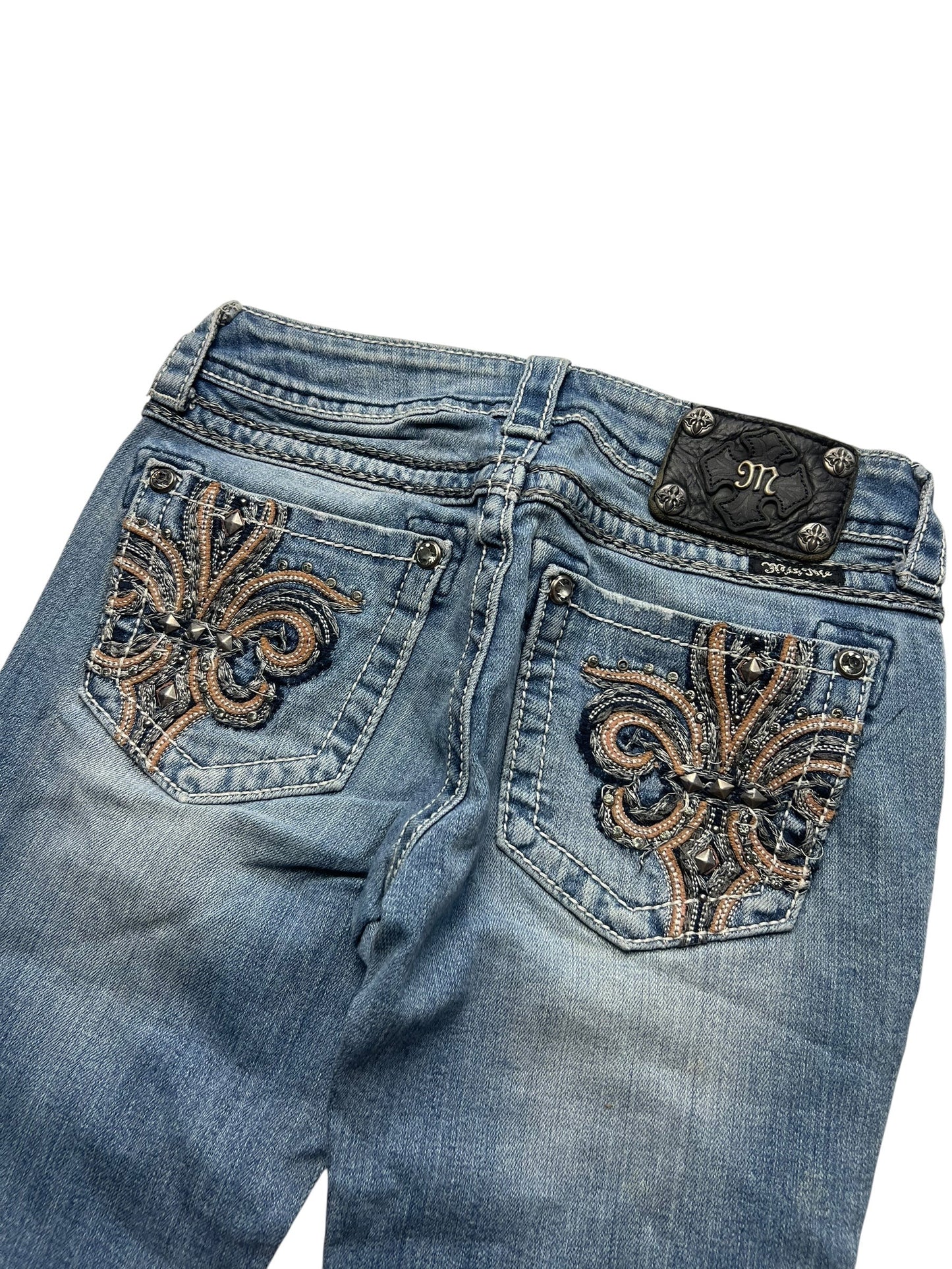 Die Miss Me Low Rise Boot-Jeans von ZAZA resell (Größe 26, S) hat einen verblassten blauen Denim, eine Fleur-de-Lis-Stickerei mit Strasssteinen auf den Gesäßtaschen und einen schwarzen Lederaufnäher mit einem M-Logo aus Metall. Überprüfen Sie Labelgröße und Bundweite für die perfekte Passform.
