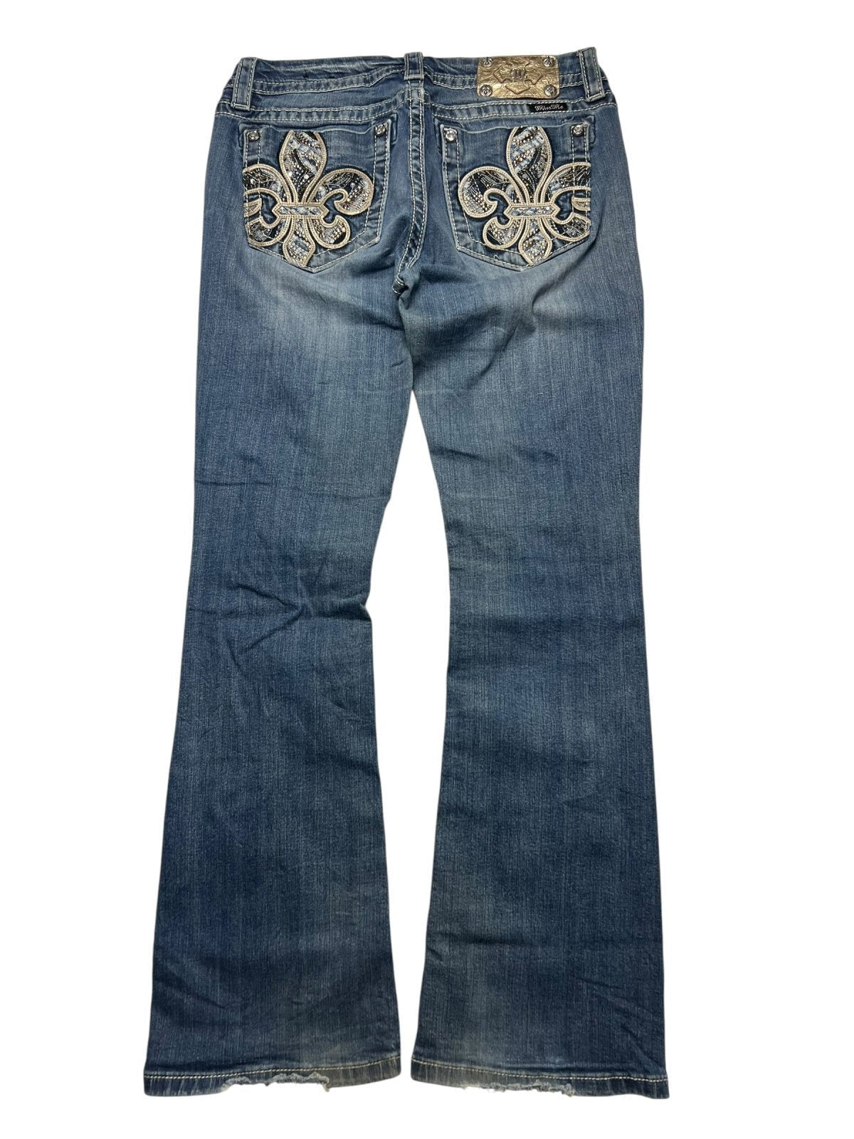 Die ZAZA resell Miss Me Mid Rise Boot in Größe 30 (M) präsentiert eine blaue Bootcut-Jeans mit großer Fleur-de-Lis-Stickerei auf den Gesäßtaschen, einem Marken-Lederpatch und detaillierten Bundweitenmaßen für einen perfekten Sitz.
