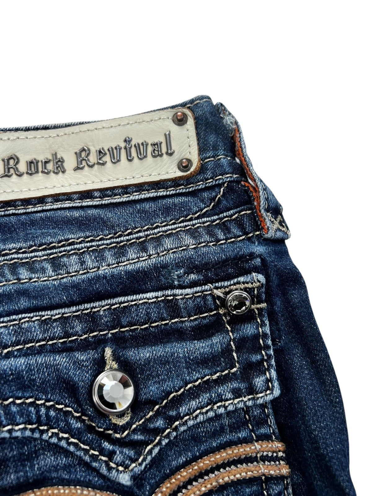 Nahaufnahme der von ZAZA weiterverkauften Rock Revival Low Rise Boot Jeans (W24 x L30) in Dunkelblau, mit hervorgehobenen Nähten, Kristallknopf, Markenetikett am Hosenbund, Bundweite und Beinöffnung, alles vor weißem Hintergrund.