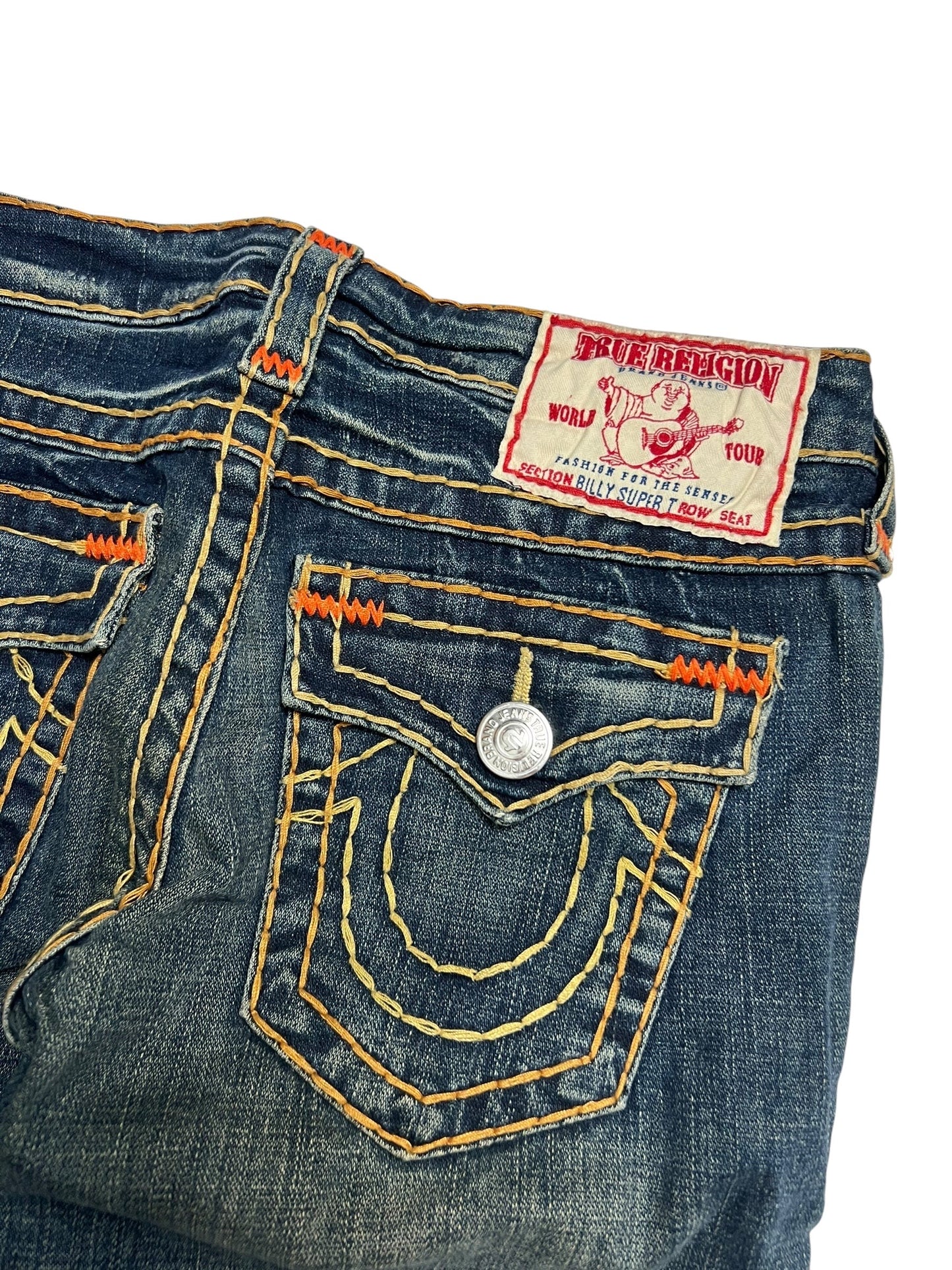 Eine Nahaufnahme der True Religion Billy Super T Jeans von ZAZA resell in Größe 27 (M), mit blauem Denim, Gesäßtasche mit gelben Nähten, orangefarbenem Markenaufnäher am Bund und detaillierten Maßen an der Taille und am Beinabschluss für eine perfekte Passform.