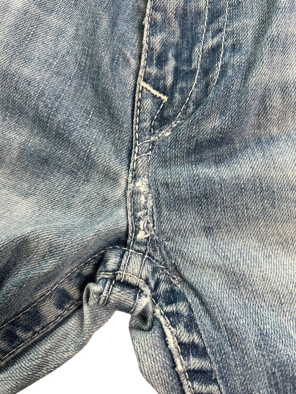 Nahaufnahme des abgenutzten Stoffs und der sichtbaren Nähte im Schritt der True Religion Straight Jeans von ZAZA resell (Größe 36/XL), mit Ausfransungen, Reparaturspuren und einem Teil der Labelgröße in der Nähe des Bunds.