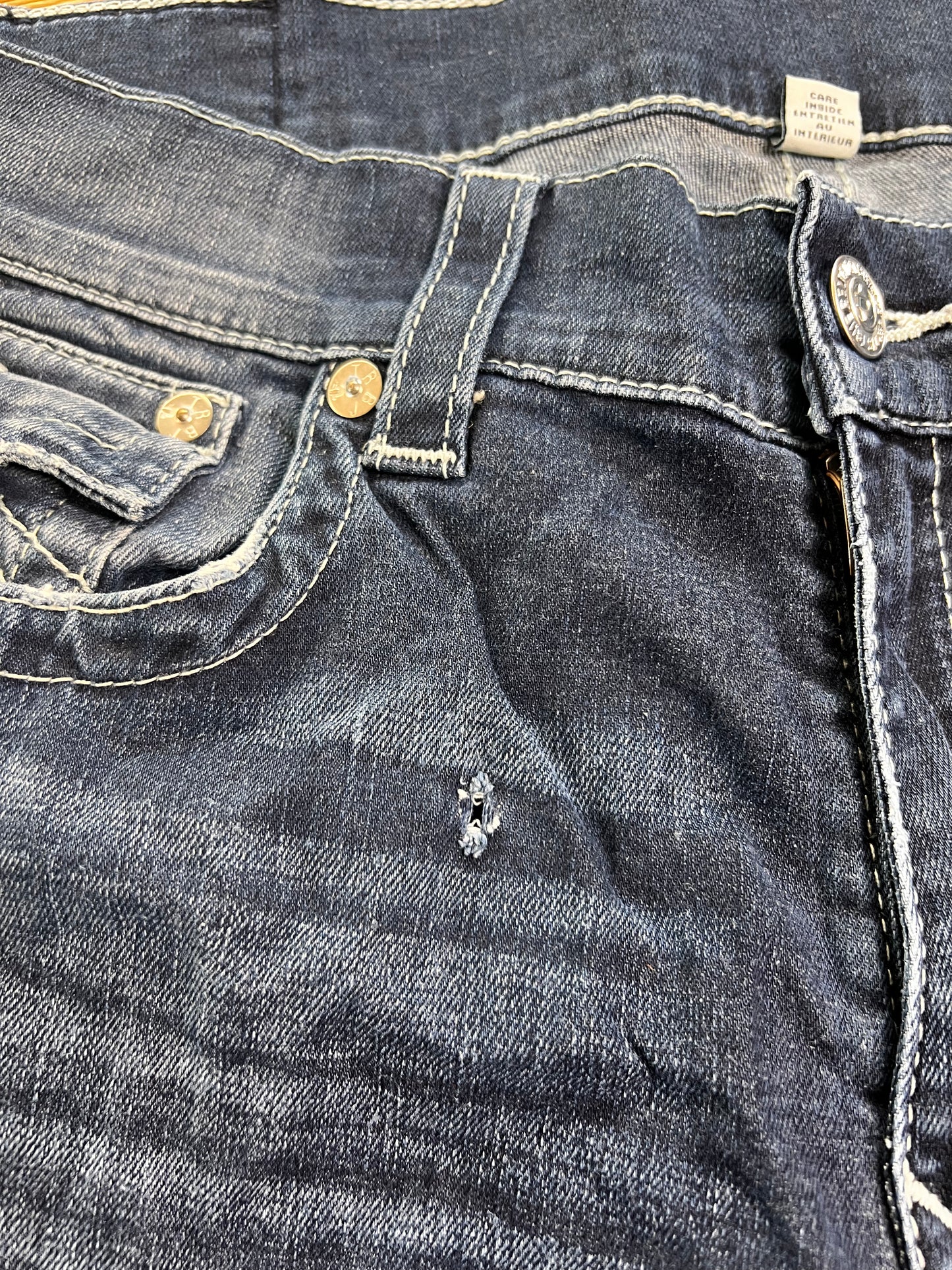 Eine Nahaufnahme der True Religion Straight Jeans (W36 x L36) von ZAZA Resell zeigt die Vordertasche, den Knopf, die Gürtelschlaufe und eine kleine Reparatur in der Nähe der Tasche; der Stoff ist abgenutzt und leicht verblasst – „Zustand“ weist auf sanften Gebrauch hin.