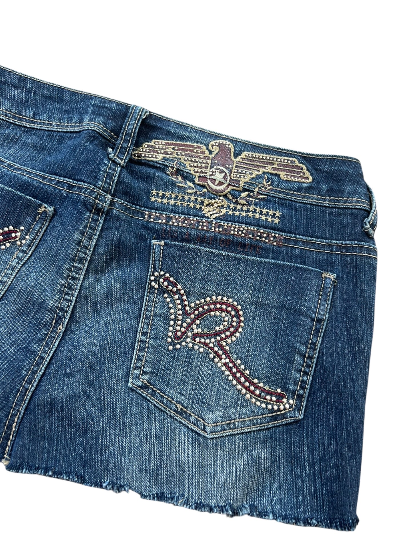 Der Rocawear Skirt | W27 von ZAZA Resell verfügt über Strass-Adler- und R-Details an der Gesäßtasche und am Hosenbund, einen ausgefransten Saum sowie Angaben zu Bundweite und Außenbeinlänge.