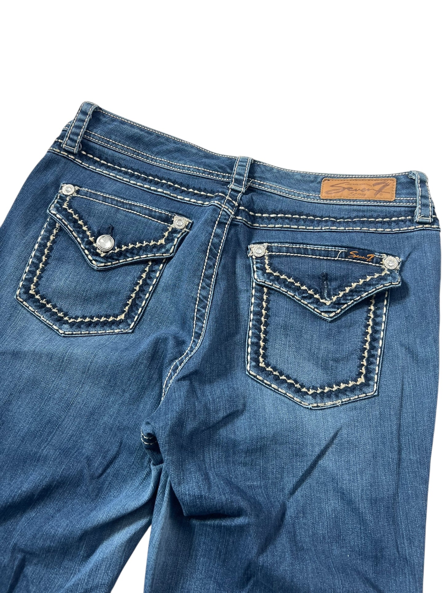 Seven Mid Rise Boot Jeans von ZAZA in den Größen W33 x L34, mit blauem Denim, weiß genähten Gesäßtaschen, silbernen Knöpfen und einem braunen Lederpatch am Bund. Die Jeans wird flach mit der Rückseite nach oben gezeigt, um die Passform leicht zu überprüfen.