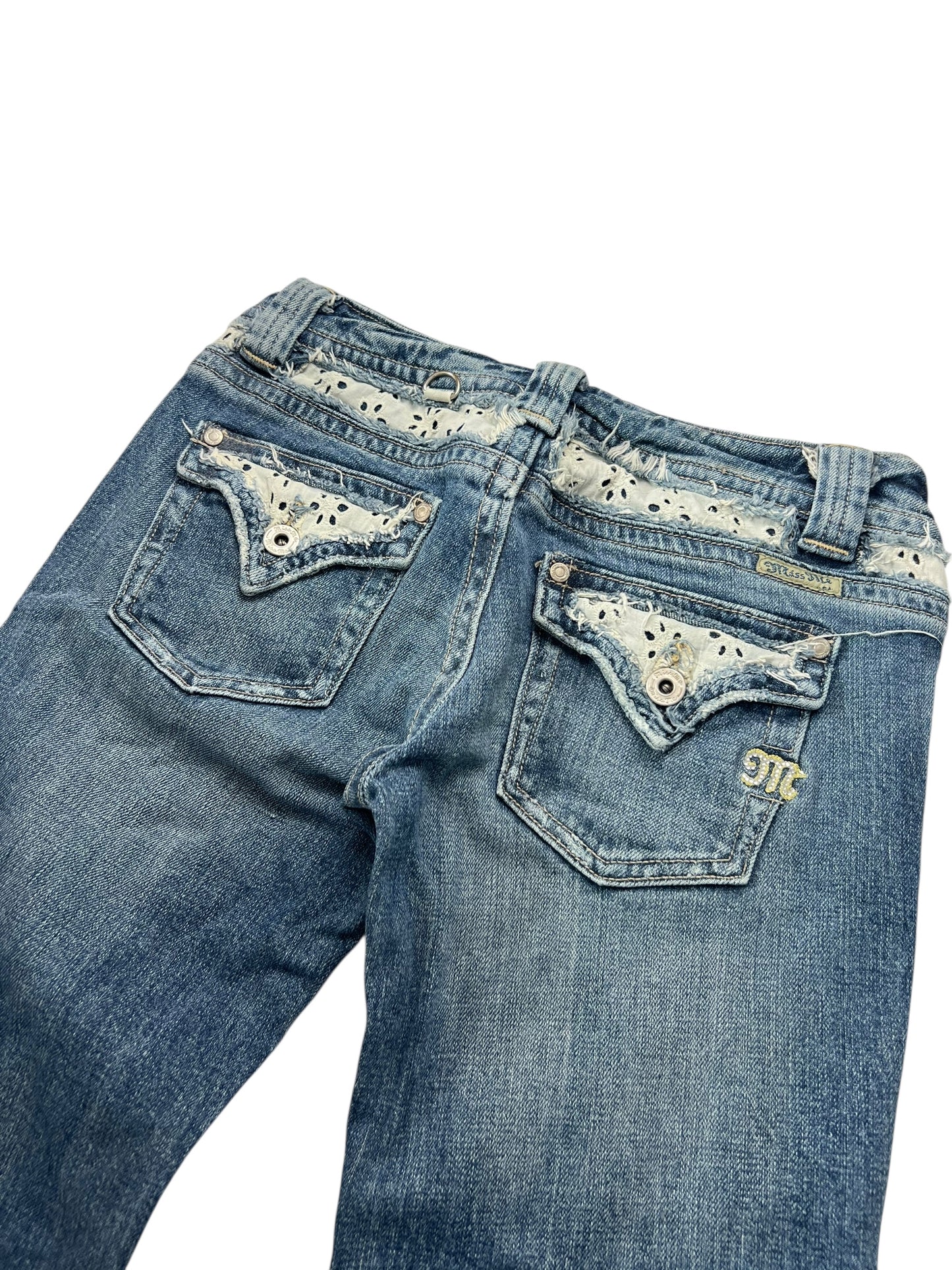Die Miss Me Low Rise Boot Jeans von ZAZA resell (W26 x L31) ist ein blauer Denim mit Ösen-Spitzenbesatz am Bund und an den Taschen, Ziernähten, Metallknöpfen, einem gestickten JTC-Patch über der Gesäßtasche und einer stylischen Beinöffnung.