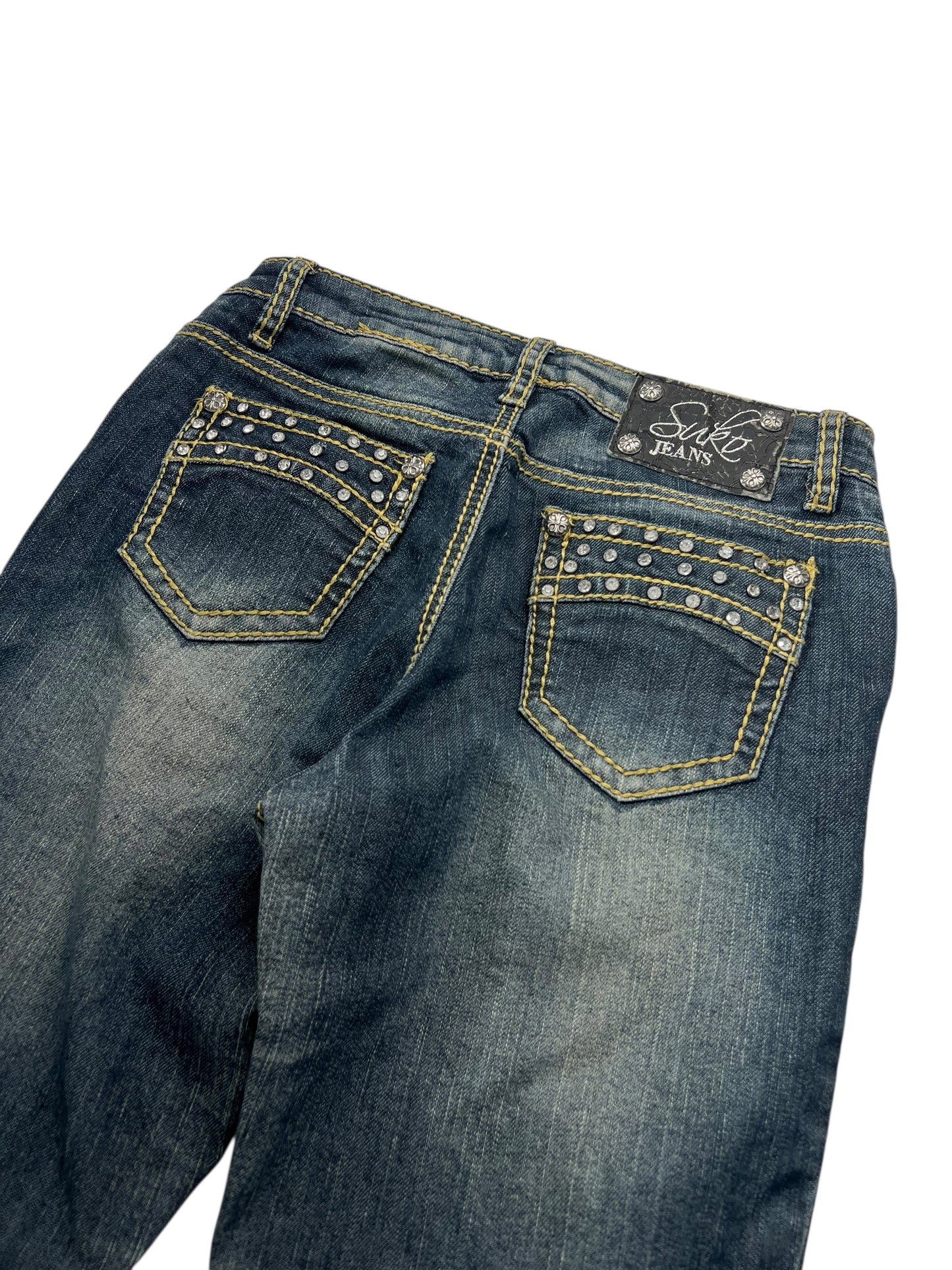 Der von ZAZA weiterverkaufte Suko Jeans Mid Rise Boot (W26 x L34) besteht aus dunkelblauem Denim, hat gelbe Nähte, mit Silbernieten besetzte Gesäßtaschen, eine bequeme Bundweite und ein schwarzes „Style Jeans“-Etikett über der rechten Tasche.