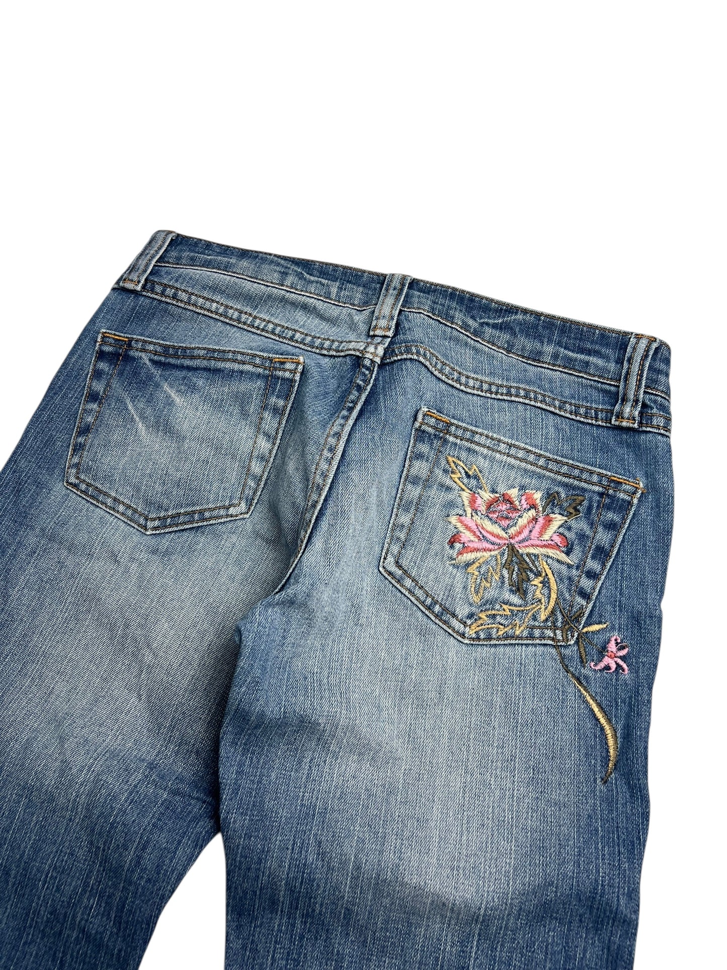 Y2K Low Rise Boot Jeans von ZAZA aus blauem Denim mit verwaschenem Used-Look und zwei Gesäßtaschen. Die rechte Tasche ist mit einer rosa Rose und grünen Blättern bestickt. Etikettengröße, Taillenumfang und Länge (B26 x L30) finden Sie in der Größentabelle.