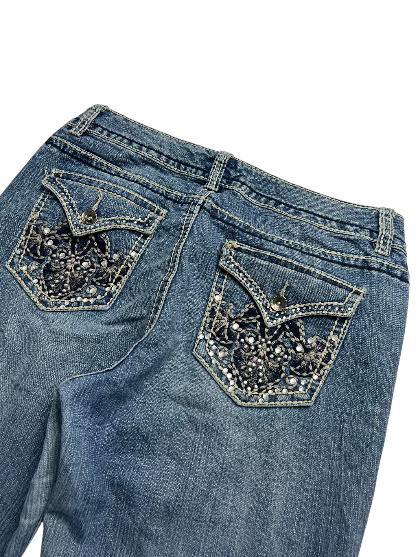 Die Nine West Mid Rise Boot Jeans von ZAZA Resell (W31 x L33) besteht aus blauem Denim mit Stickereien und Perlenmustern auf den hinteren Pattentaschen mit Metallknöpfen. Flach auf weißem Hintergrund platziert, um Bundweite und stilvolle Details hervorzuheben.