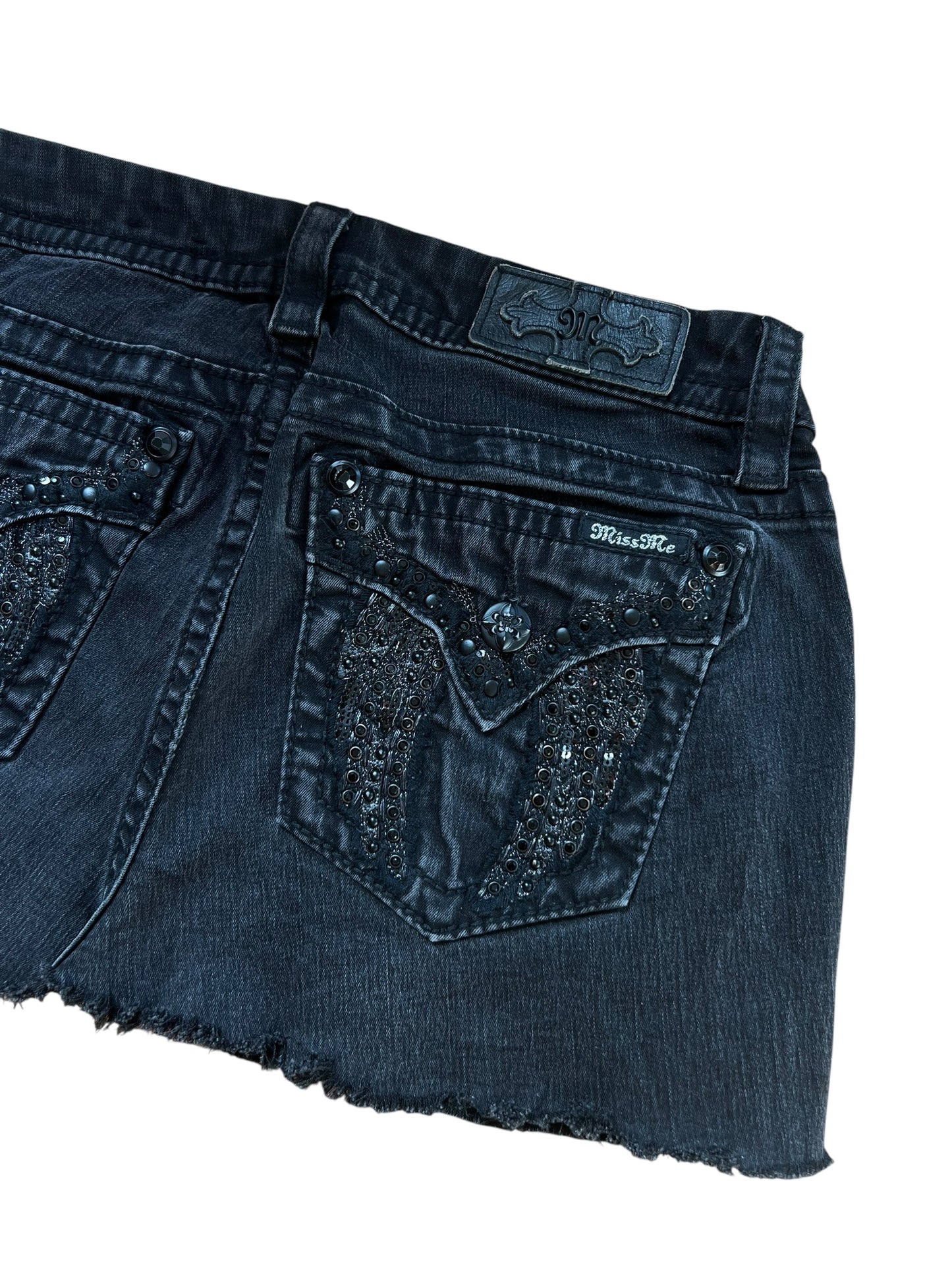 Miss Me Rock von ZAZA resell in Größe 29 (M), mit schwarzem Denim, rohem Saum, Ziernähten, Strasssteinen und einer Pattentasche hinten. Etikett und Größe sind oberhalb der Tasche sichtbar. Flach gelegt, Taille misst 39 cm auf weißem Hintergrund.