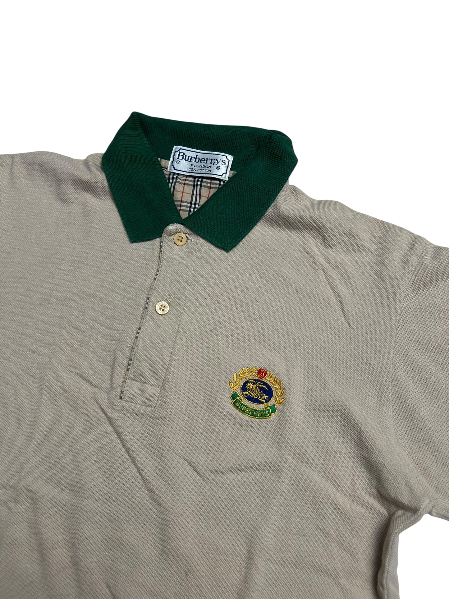 Burberry Polo Shirt | S von ZAZA resell in beige mit grünem Kragen, zwei Knöpfen und gesticktem Wappenlogo auf der linken Brust. Innenkragen mit Burberry-Etikett und Signatur-Karo. Zustand 9/10. Maße in cm auf Anfrage.