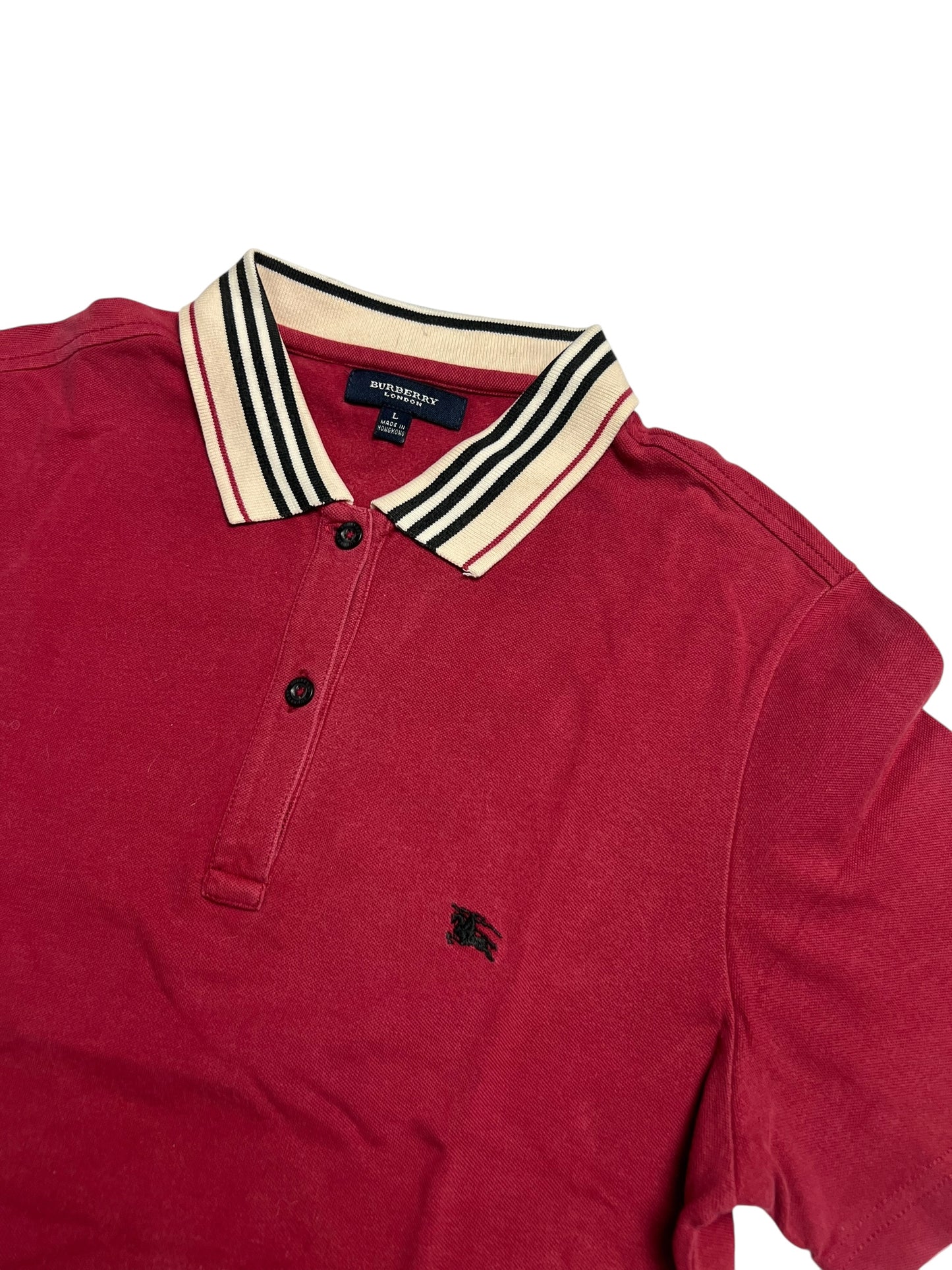 Ein Burberry Polohemd (M) von ZAZA resell, mit rotem Körper, beige-schwarz gestreiftem Kragen, schwarzen Knöpfen und Burberry-Logo auf der linken Brust. Etikettengröße L, Zustand 9/10. Flach auf einem weißen Hintergrund gelegt.