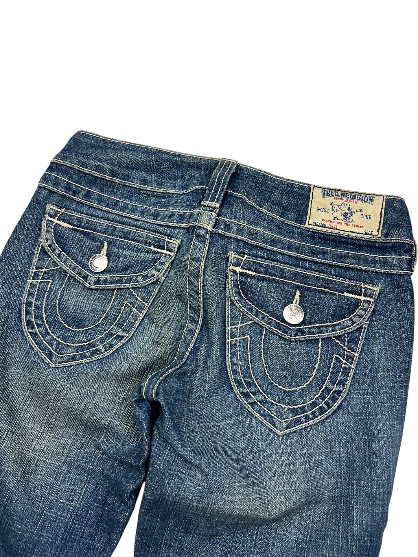 Eine Nahaufnahme der Rückseite der True Religion Skinny Jeans (Größe 25/S) von ZAZA resell aus blauem Denim mit weißen Nähten, Pattentaschen mit Knopfverschluss, einem Markenaufnäher am Bund und einem Labelgrößen-Tag in der Nähe des Größenbereichs.