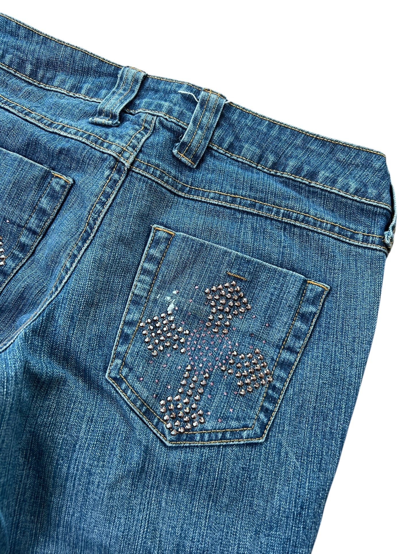 ZAZA verkauft L.E.I. Ashley Ultra Low Rise Boot Jeans, W25 x L30: blauer Denim mit bundweitem Bund, Strass-Kreuzdetail auf der Gesäßtasche, leichtes Verblassen, sichtbare Nähte, Gürtelschlaufen; abgebildet auf schlichtem weißem Hintergrund.
