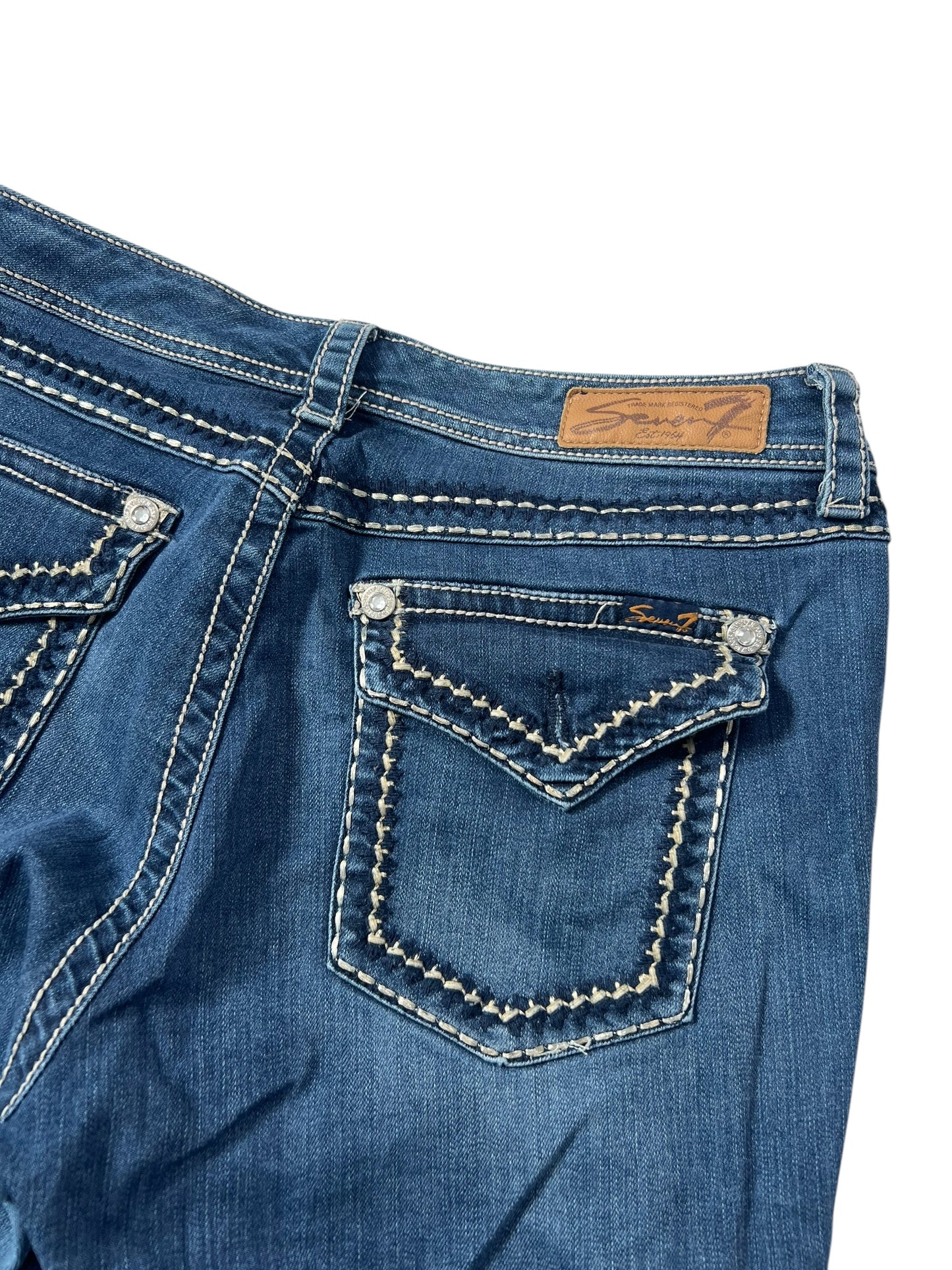Eine Nahaufnahme der von ZAZA weiterverkauften Seven Mid Rise Boot Jeans (W33 x L34) in blauem Denim mit weißen Nähten an Taschen und Säumen, einem braunen Lederpatch über der rechten Gesäßtasche und Bundweite-Details für eine perfekte Passform.