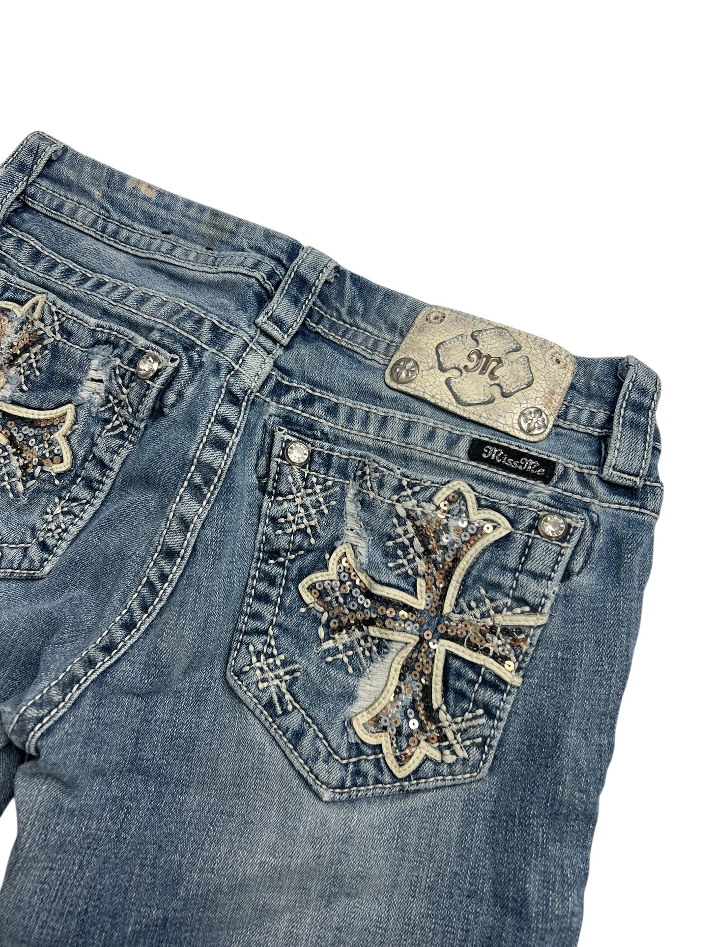Eine blaue Miss Me Mid Rise Boot Jeans (W28 x L26) von ZAZA Resell mit gestickten und mit Pailletten besetzten Kreuzmustern auf den Gesäßtaschen, Metallnietenakzenten und einem Marken-Lederaufnäher für eine stylische Passform.