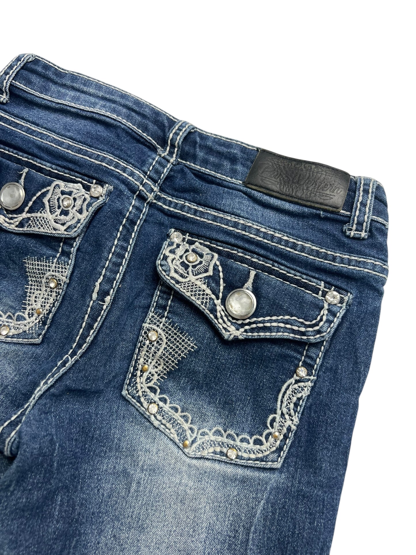 Eine Nahaufnahme der Rückseite der ZAZA-Resell-Jeans Pure Western Mid Rise Slim Boot (W23 x L26) in Kindergröße mit Ziernähten, silbernen Knöpfen, Spitzentaschen-Akzenten und einem schwarzen Lederpatch am Hosenbund.