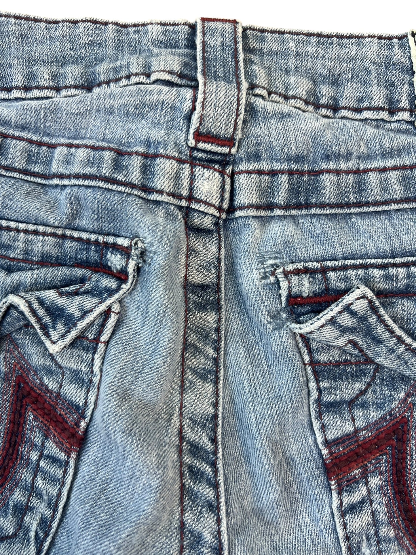 Nahaufnahme des hinteren Bunds und der Taschen der True Religion Shorts | 25 (XS) von ZAZA resell, mit blauem Denim, roten Ziernähten, einem Teil einer Gürtelschlaufe und zwei aufgenähten Gesäßtaschen. Bundweite 33 ist bekannt für individuelle Größenanpassung.