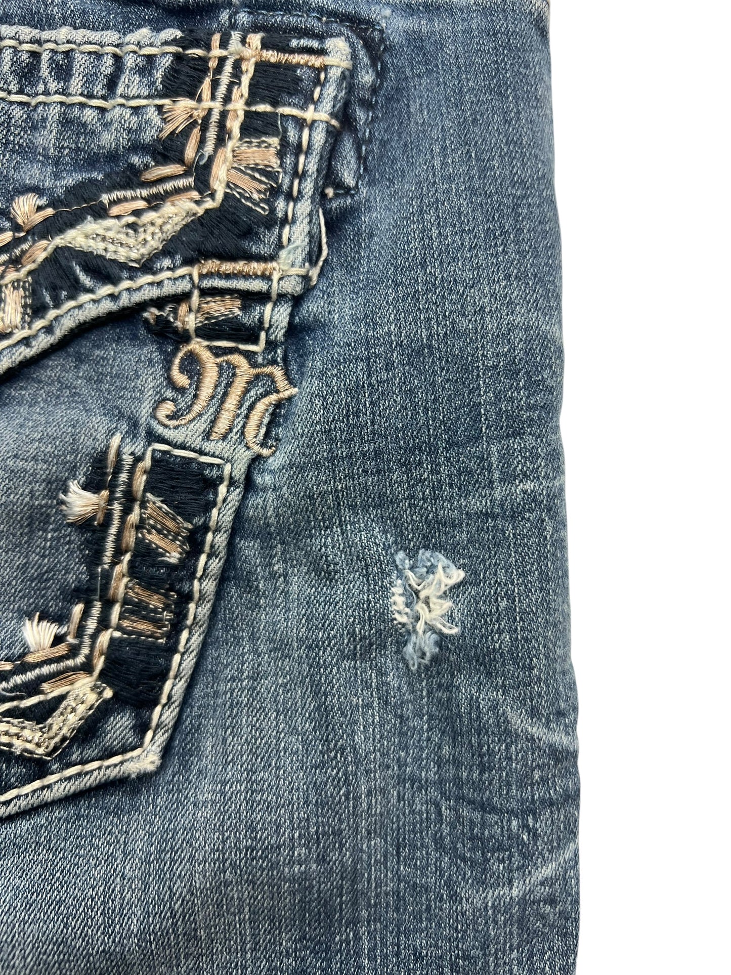 Eine Nahaufnahme der ZAZA resell Miss Me Mid Rise Curvy Boot Jeans in Größe 28 (M) zeigt die Gesäßtasche mit Ziernähten, ein kleines ausgefranstes Loch, klassische Details und eine schmeichelhafte Passform für Kurven in strapazierfähigem blauem Denim.