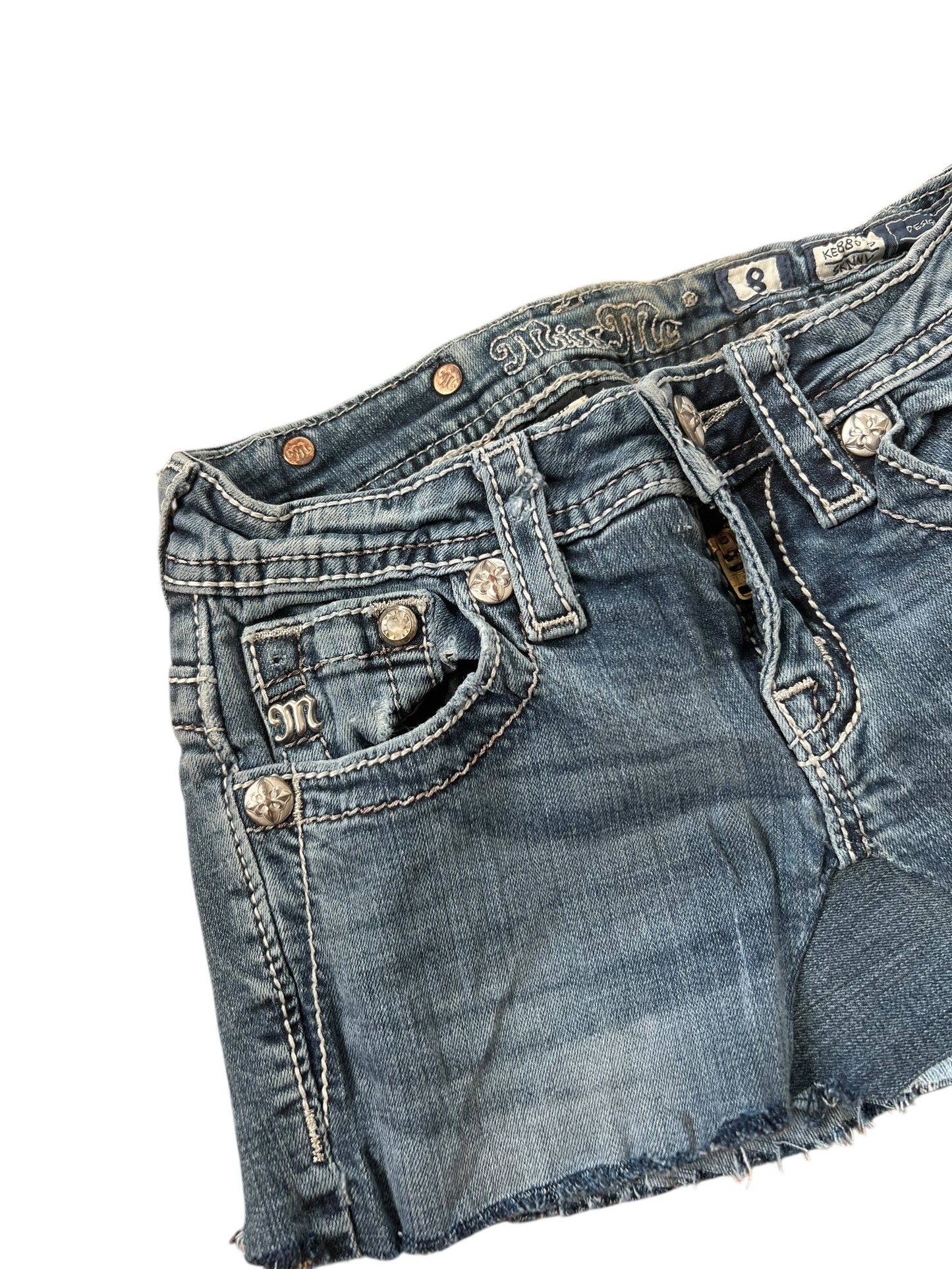 Ein blauer Miss Me-Jeansrock (XXXS) mit ausgefransten Säumen und detailreichen Nähten. Silberne Knöpfe und ZAZA-Wiederverkaufs-Branding am Bund; erhältlich in Kindergrößen oder individuellen Maßangaben in Zentimetern.