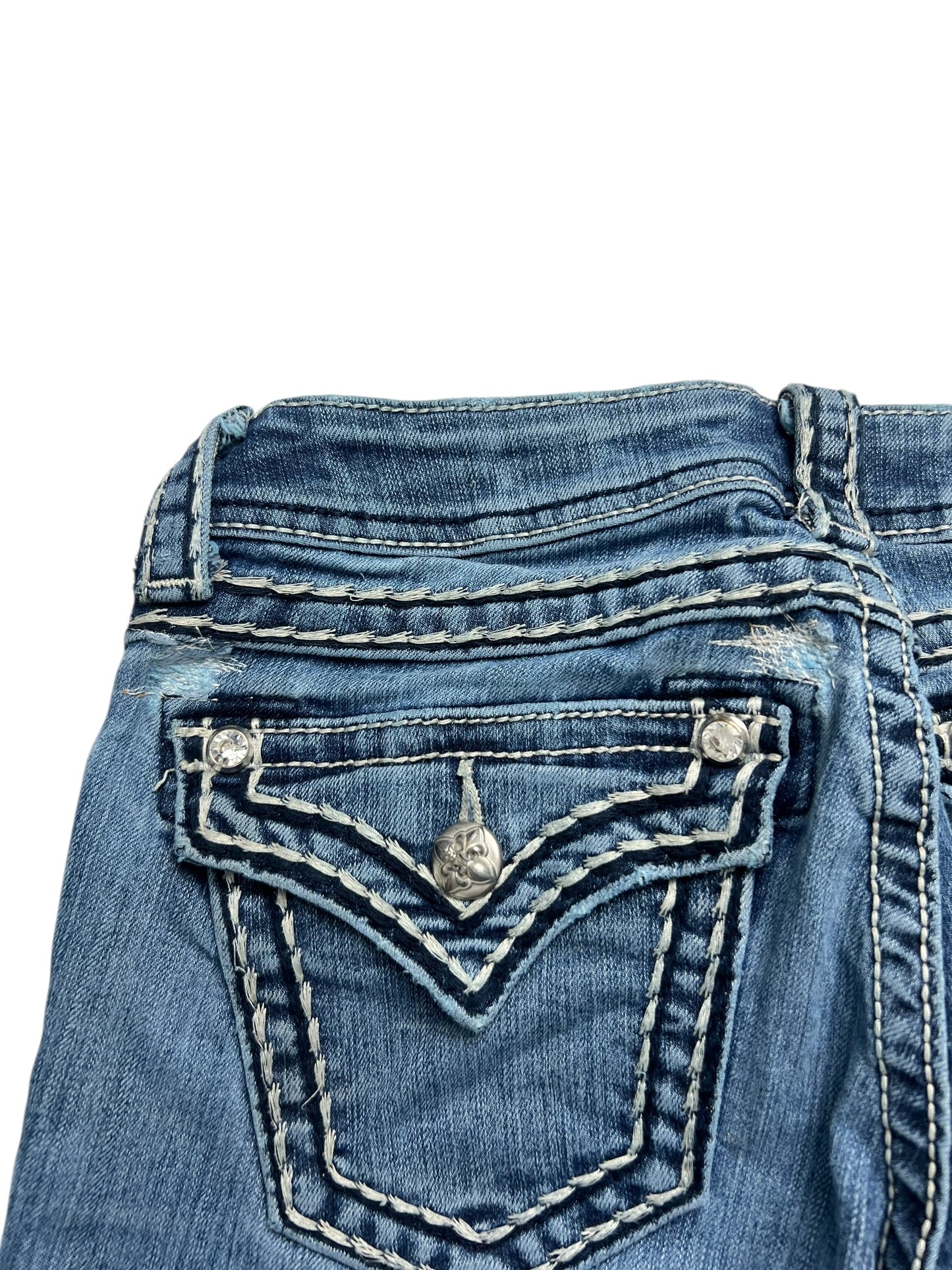 Nahaufnahme der Gesäßtasche der Jeans „Miss Me Low Rise Boot“ (W25 x L30) von ZAZA Resell, aus blauem Denim im Used-Look mit dicken weißen Nähten und einem silbernen Knopf auf der Taschenklappe.
