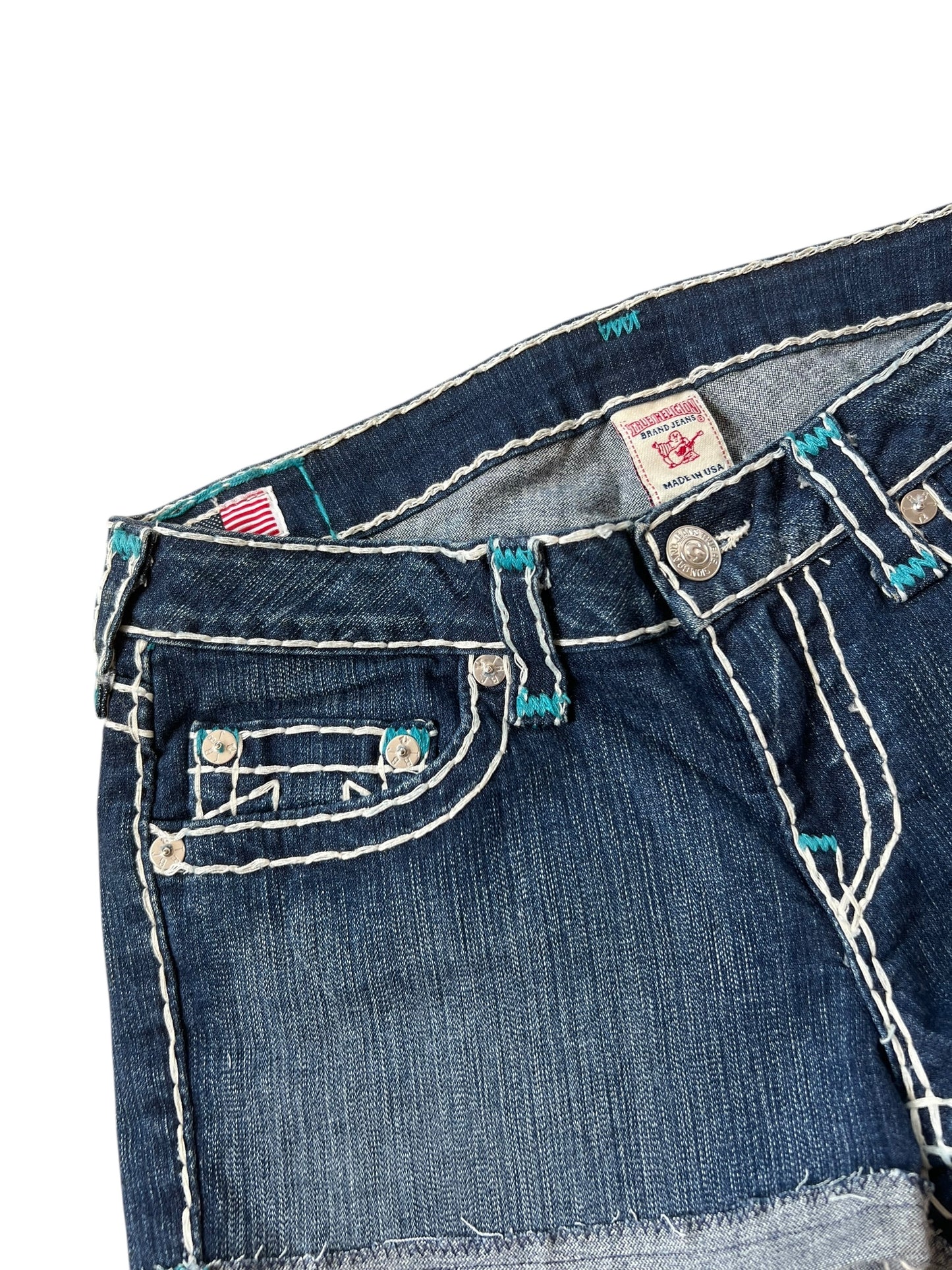 Nahaufnahme des Oberteils der True Religion Shorts von ZAZA resell, Größe 30 (M), mit weißen Nähten, Vordertasche, Knopfleiste und Bundetikett. Mit leicht abgenutztem Finish für einen lässigen Look.