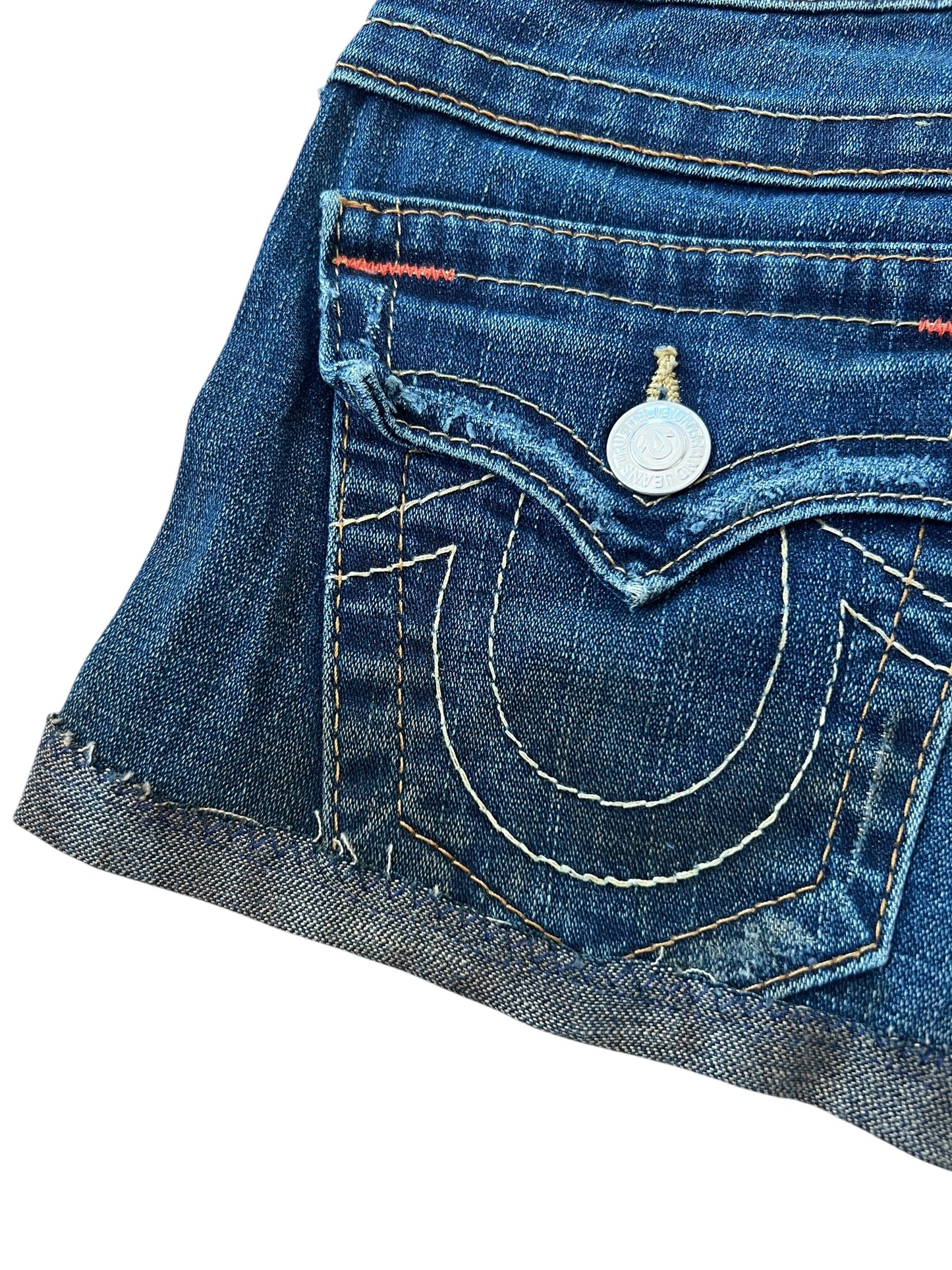 Eine Nahaufnahme der True Religion Shorts | 23 (XS) von ZAZA resell zeigt eine Gesäßtasche aus blauem Denim mit weißen und gelben Nähten, einen silbernen Knopf, rote Akzente am Bund und ein geschwungenes Design für einen klassischen Cowboy-Stil.