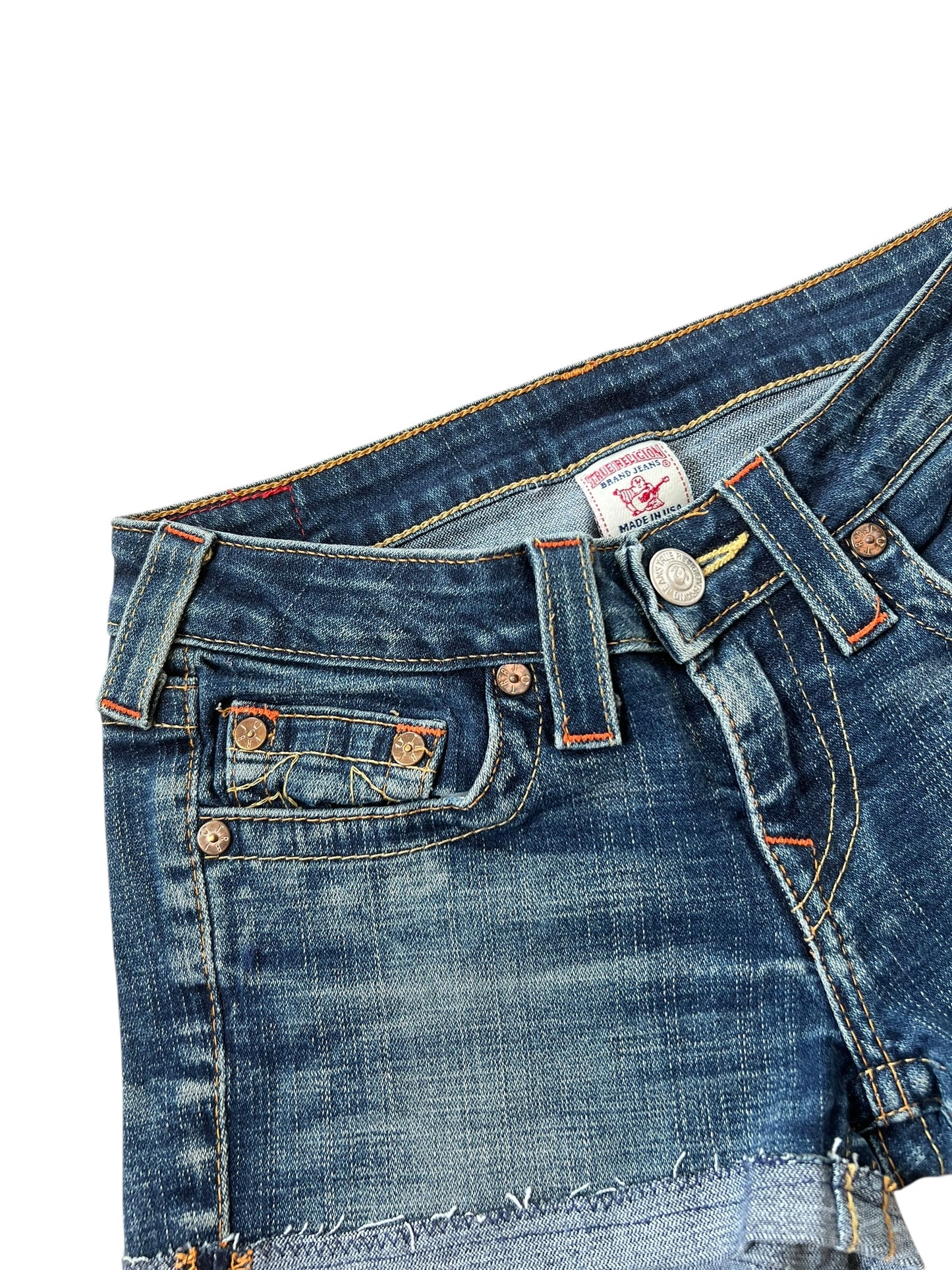 Eine Nahaufnahme der True Religion Shorts von ZAZA resell aus blauem Denim mit kupfernen Nieten, einem Metallknopf, sichtbaren Nähten, einer verblassten Struktur und Etikettendetails: Größe 27 (S).