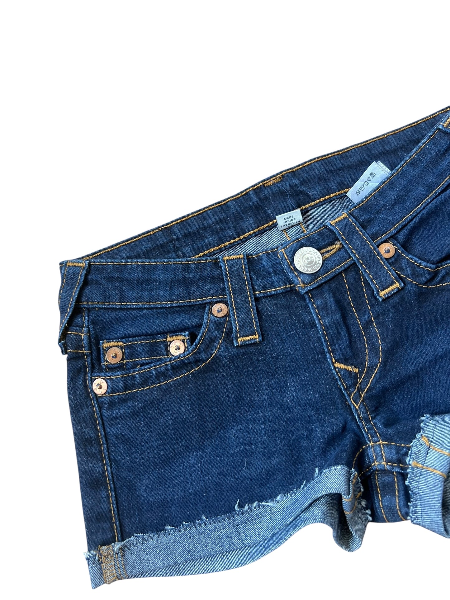True Religion Shorts | 24 (XS) von ZAZA resell aus dunkelblauem Denim mit aufgerollten, ausgefransten Säumen und kupferfarbenen Nieten, teilweise auf weißem Grund. Bundweite 33.
