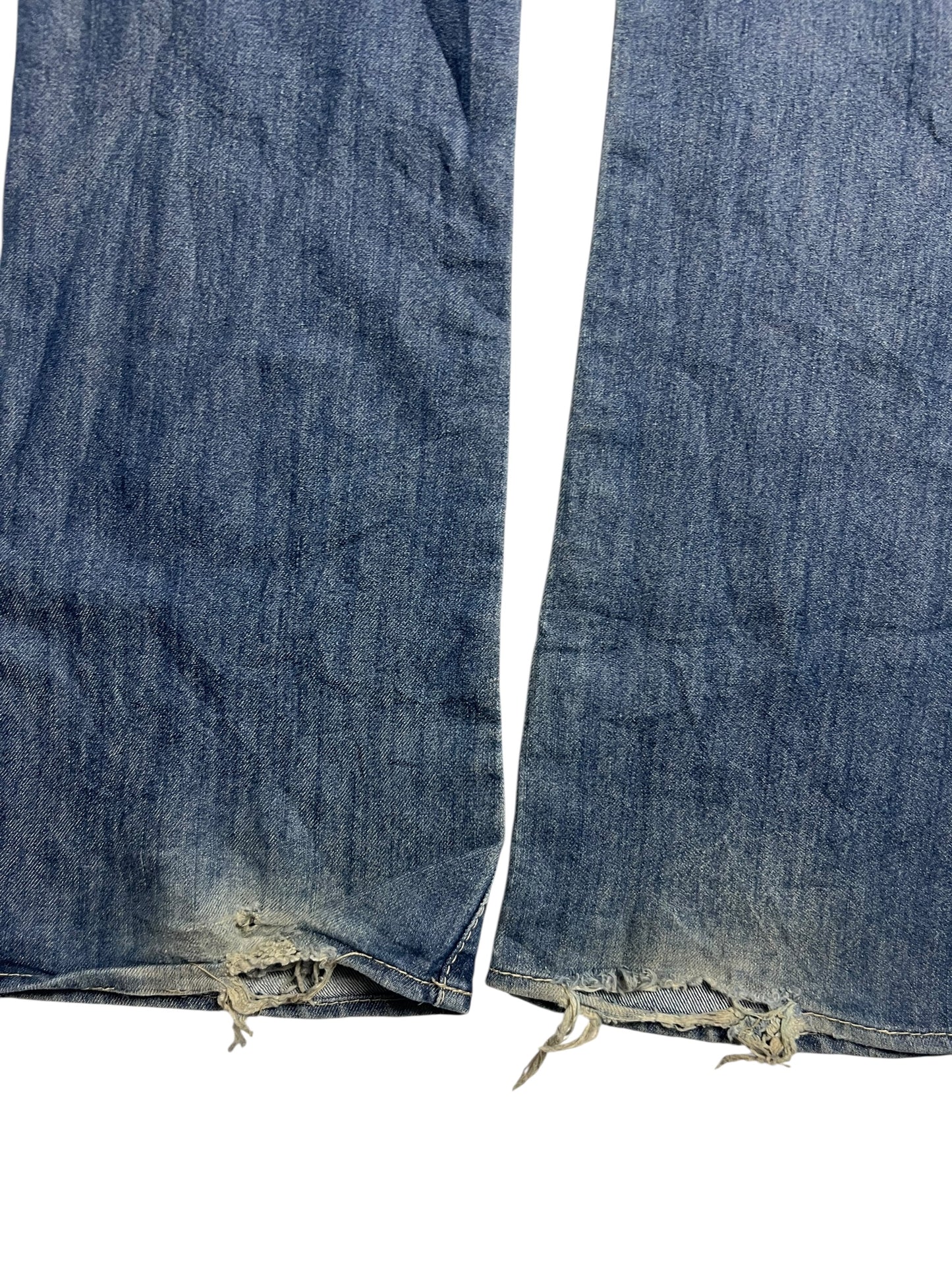 Eine Nahaufnahme der Apple Bottoms Mid Rise Boot Jeans von ZAZA resell, die hochwertiges Material mit ausgefransten, abgenutzten Säumen, losen Fäden und leichten Randverfärbungen vor einem weißen Hintergrund zeigt.
