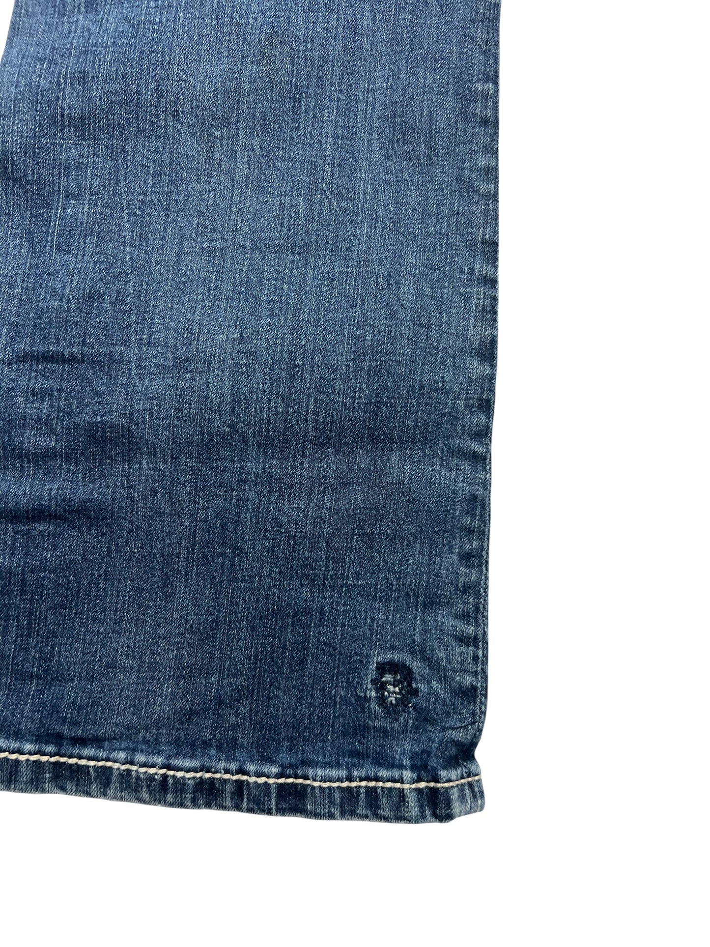 Nahaufnahme der Miss Me Mid Rise Curvy Boot Jeans (28/M) von ZAZA resell. Sie zeigt blauen Denim, einen leicht ausgefransten Saum, einen kleinen kreisförmigen, abgenutzten Fleck in der Nähe der Kante und eine taillierte Bundweite für zusätzlichen Komfort.