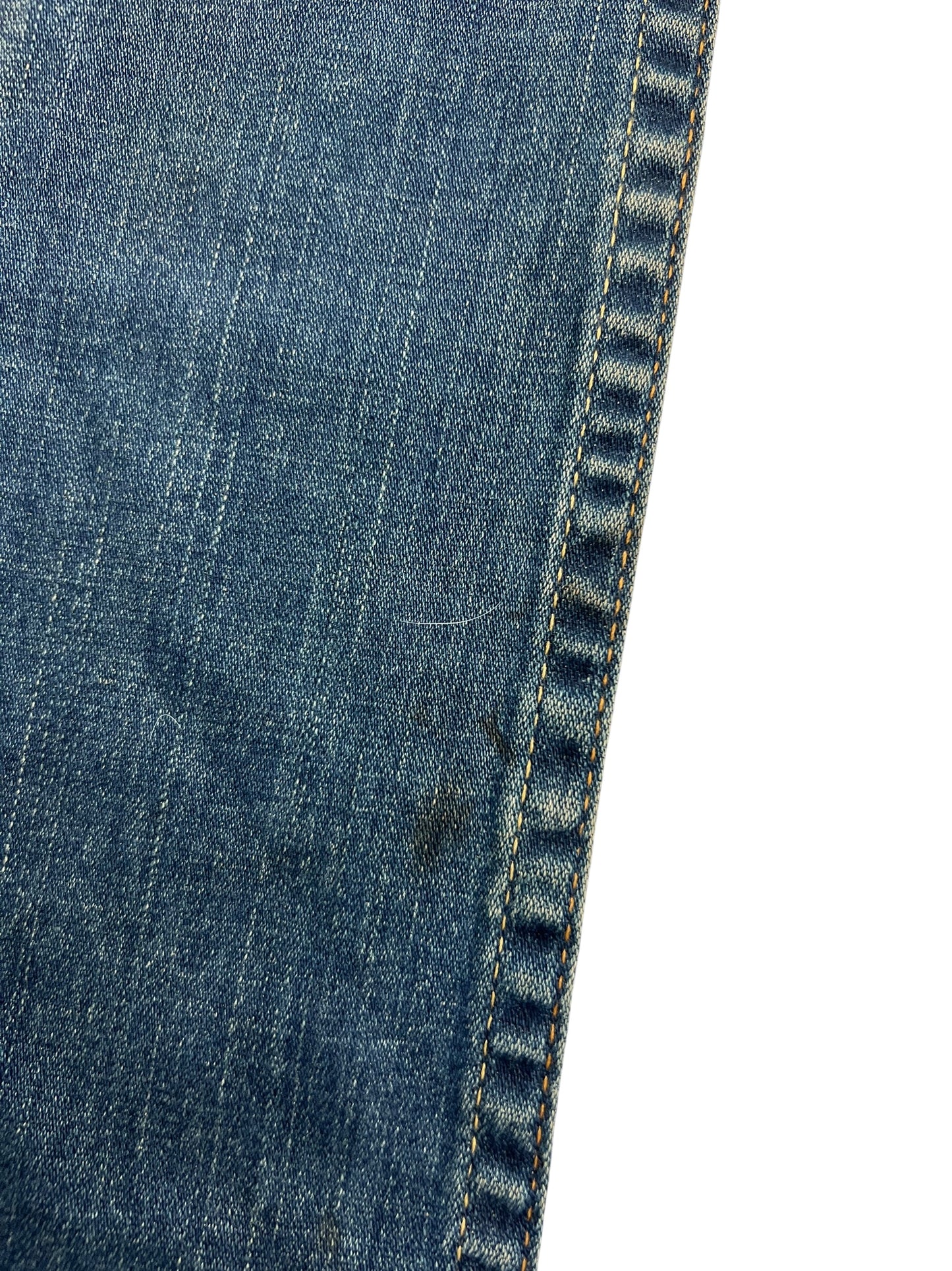 Nahaufnahme von blauem Denim-Stoff mit gelben Nähten und einem kleinen Fleck in der Nähe der Naht. Die True Religion Billy - Low Rise Straight | 24 (S) von ZAZA resell vereint ideale Passform und Qualität für Detailverliebte.