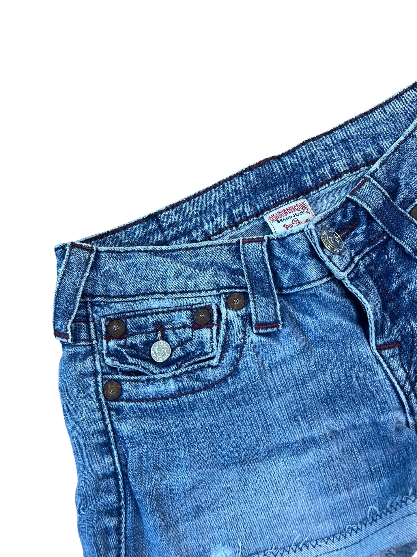 Eine Nahaufnahme des oberen Teils der True Religion Shorts | 25 (XS) von ZAZA resell, die den Bund, die Vordertaschen mit Nieten, die Gürtelschlaufen und einen Metallknopf zeigt. Die Custom Shorts sind sorgfältig genäht vor einem weißen Hintergrund.