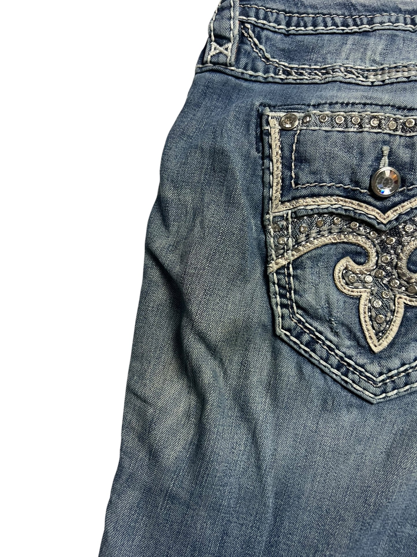 Eine Nahaufnahme der Rock Revival Mid Rise Boot | 32 (XL) Jeans von ZAZA resell zeigt einen verblichenen, abgenutzten Look und ein Oberteil mit einer bestickten, strassbesetzten Gesäßtasche. Bundweite 46 und Außenbeinlänge 110 sorgen für eine einzigartige Passform.