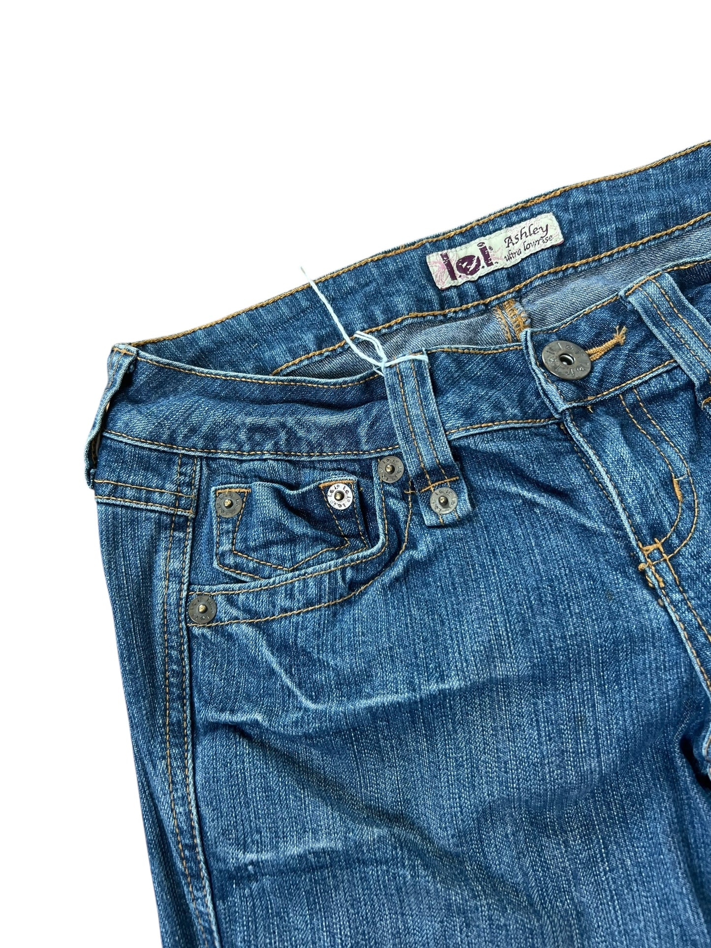 Die L.E.I. Ashley Ultra Low Rise Boot Jeans (B25 x L30) von ZAZA Resell ist aus blauem Denim gefertigt und verfügt über sichtbare Nähte, Front- und Münztaschen, Gürtelschlaufen und einen Knopfverschluss. Außenbeinlänge und Bundweite werden flach auf weißem Untergrund gemessen.
