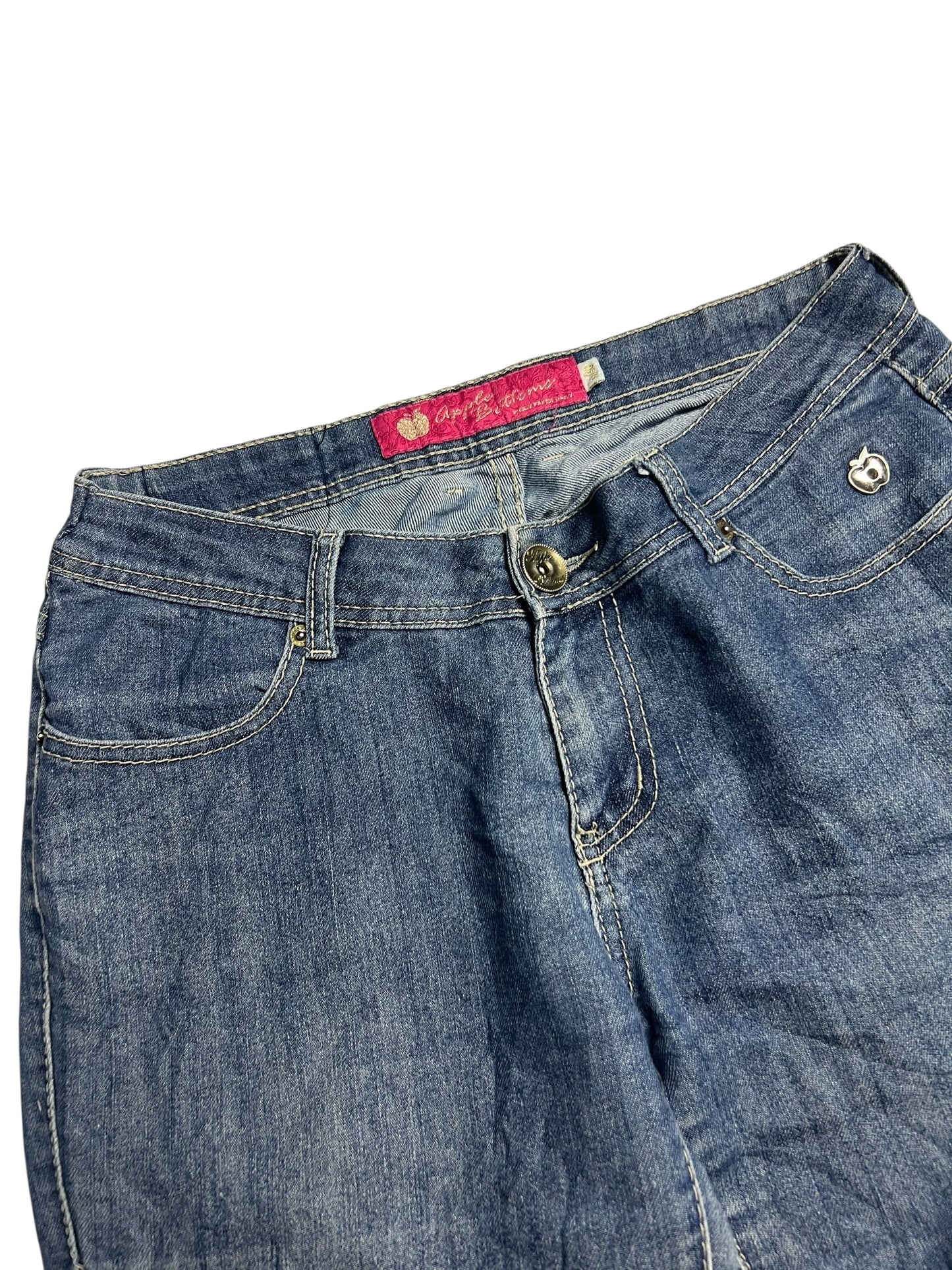 Eine Nahaufnahme der Apple Bottoms Mid Rise Boot Jeans von ZAZA resell aus blauem Denim mit Bund, Vordertaschen, Knopfverschluss und einem rosa Innenetikett. Die Jeans sind flach auf einem weißen Hintergrund abgebildet.