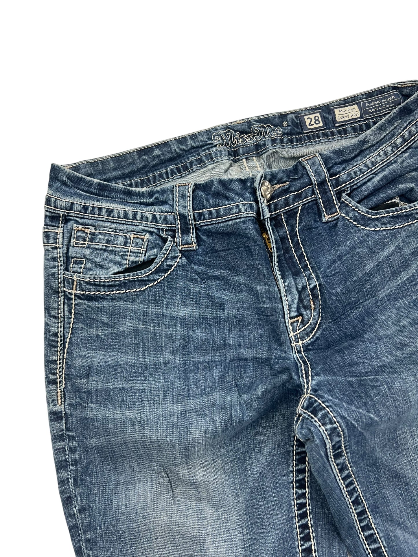 Die Miss Me Mid Rise Curvy Boot Jeans von ZAZA resell in Größe 28 (M) hat blauen Denim, weiße Kontrastnähte, Taschen vorne, Gürtelschlaufen und einen Knopfverschluss. Bundweite und Außenbeinlänge sind auf den Etiketten angegeben; ideal für kurvigere Figuren.