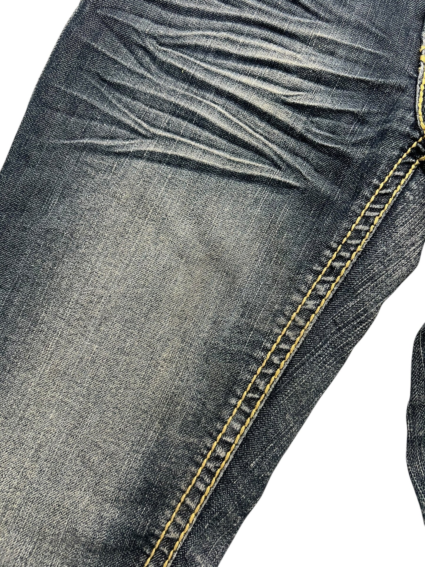 Nahaufnahme des Suko Jeans Mid Rise Boot von ZAZA Resell (W26 x L34) aus verblichenem blauem Denim mit hervorgehobenen gelben Nähten, sichtbaren Bügelfalten in der Nähe der Tasche und detaillierter Bundweite.