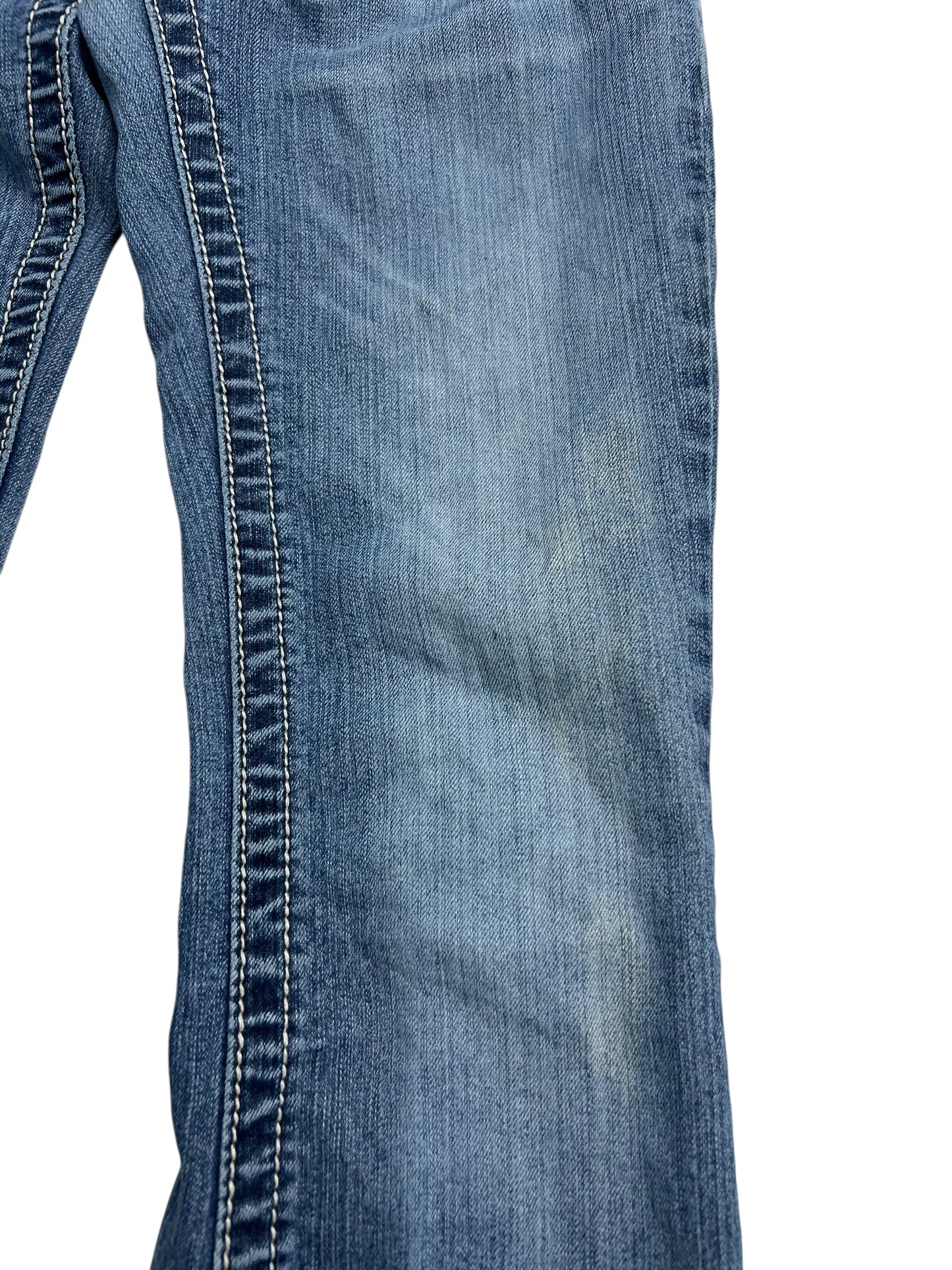 Eine Nahaufnahme der Miss Me Low Rise Boot Jeans (W25 x L30) von ZAZA Resell zeigt den Used-Look mit verblichenem blauem Denim und markanten weißen Doppelnähten entlang der Naht vor weißem Hintergrund.