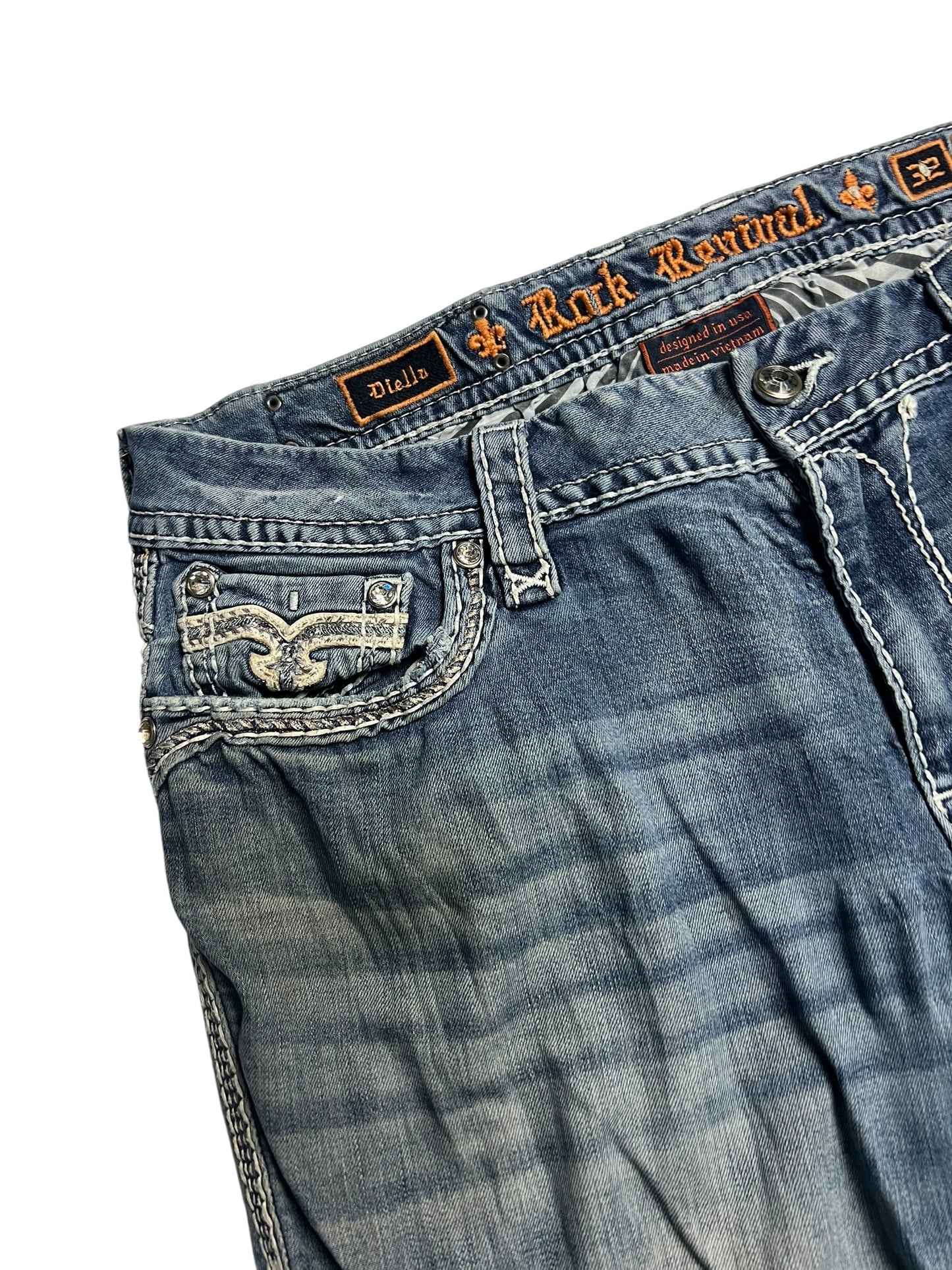 Eine Nahaufnahme der Rock Revival Mid Rise Boot Jeans (32/XL) von ZAZA resell hebt die detaillierten Nähte, die Gürtelschlaufe, die orangefarbene Markenstickerei am Bund und den leicht verblichenen, abgenutzten Look hervor.