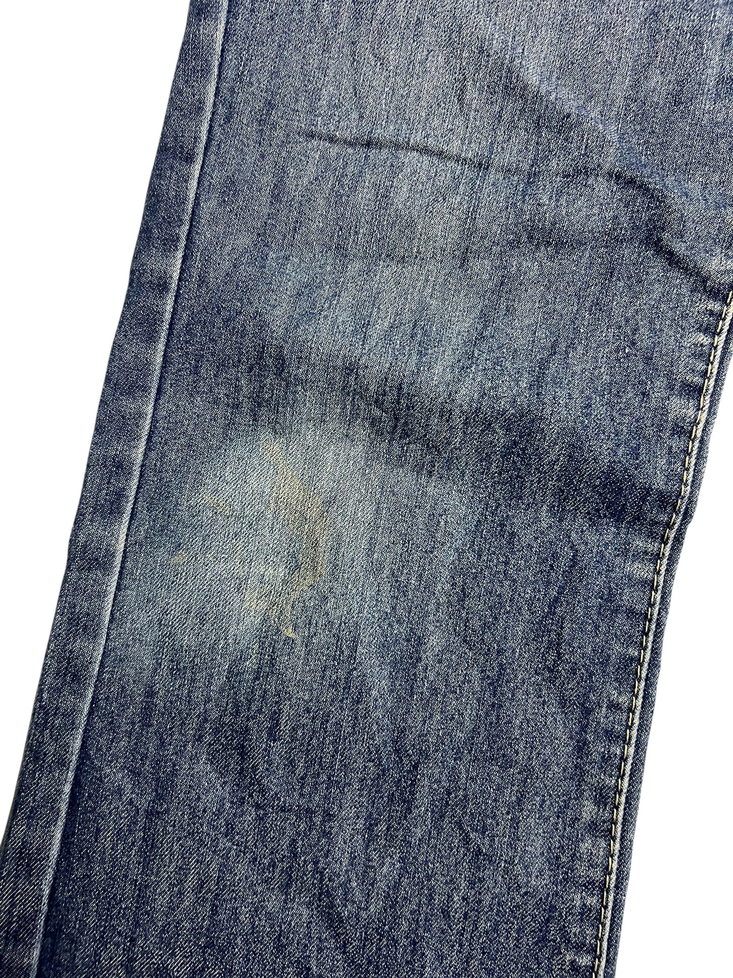 Eine Nahaufnahme der Apple Bottoms Mid Rise Boot Jeans von ZAZA resell zeigt verblichenen, abgenutzten blauen Denim in der Nähe des Knies, mit sichtbaren Nähten und Stoffdetails.